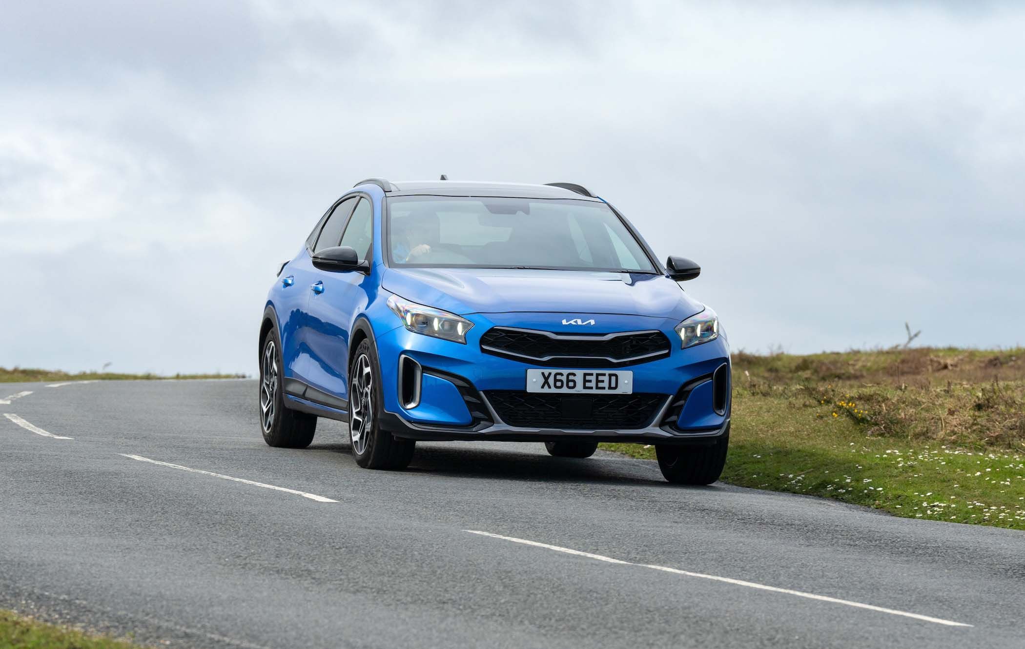 Blue Kia XCeed driving on a winding road with a cloudy sky in the background.