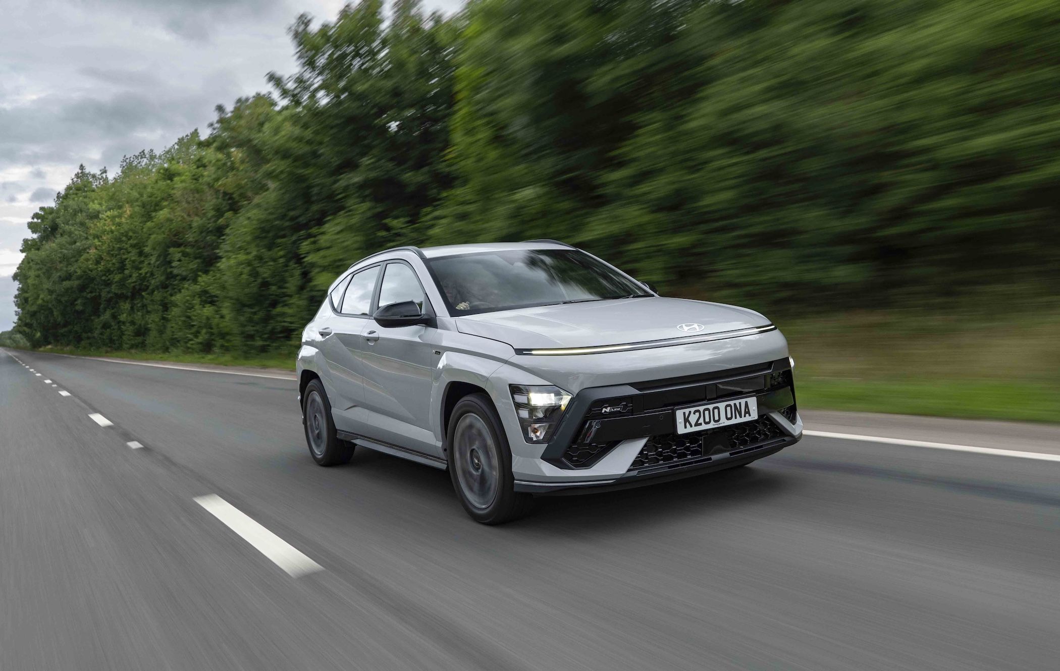Silver Hyundai KONA driving on a highway with blurred green trees in the background, conveying motion and speed.