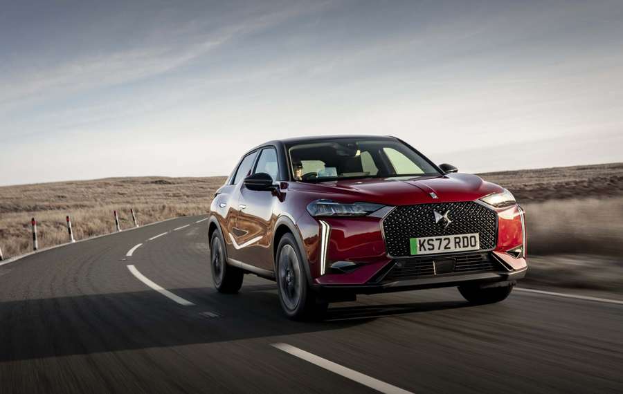 Red DS 3 driving on a winding road through a barren landscape under a clear sky.