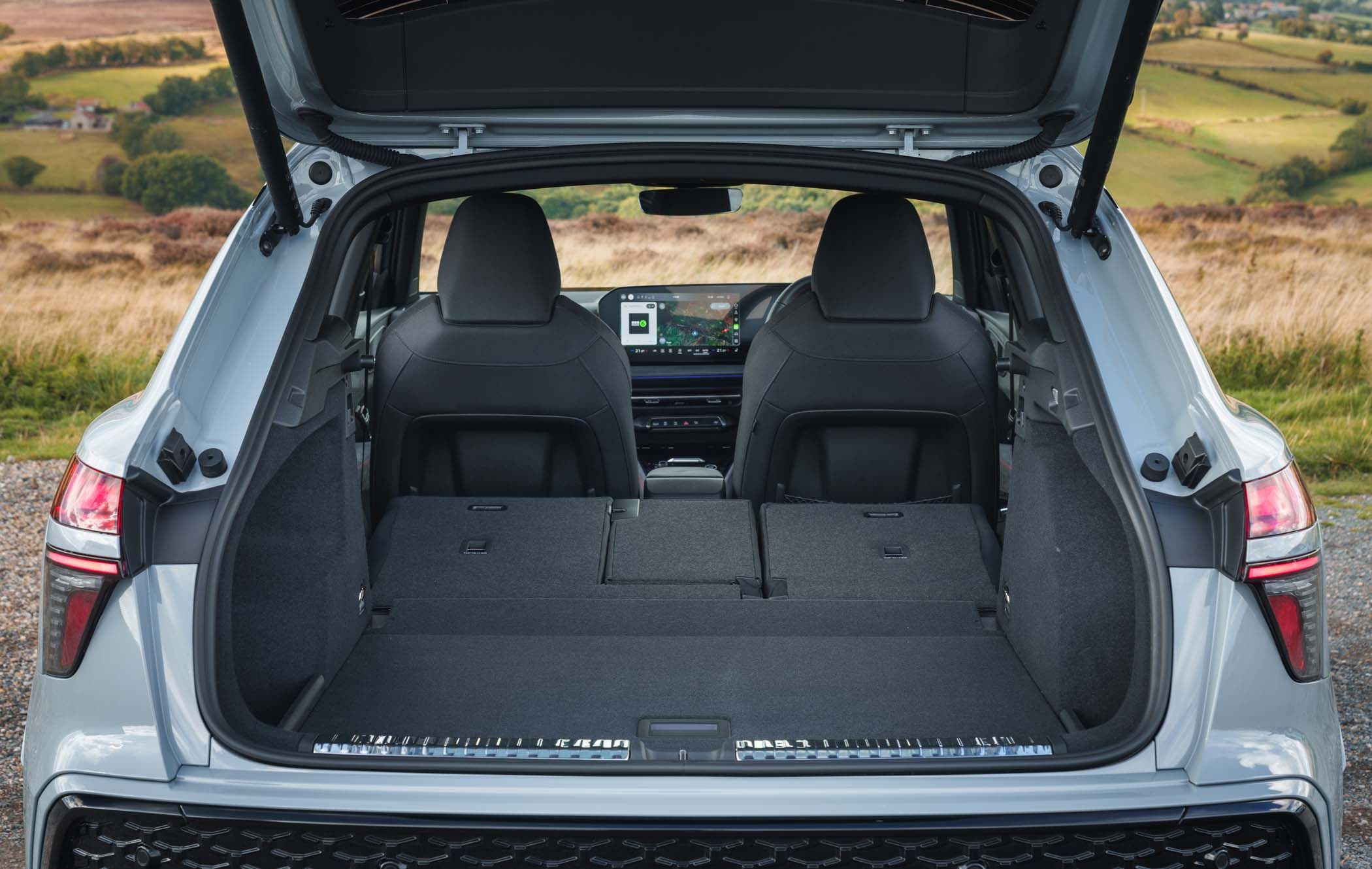 Open Audi Q3 boot with rear seats folded flat, showing spacious cargo area. Interior dashboard and countryside visible in the background.