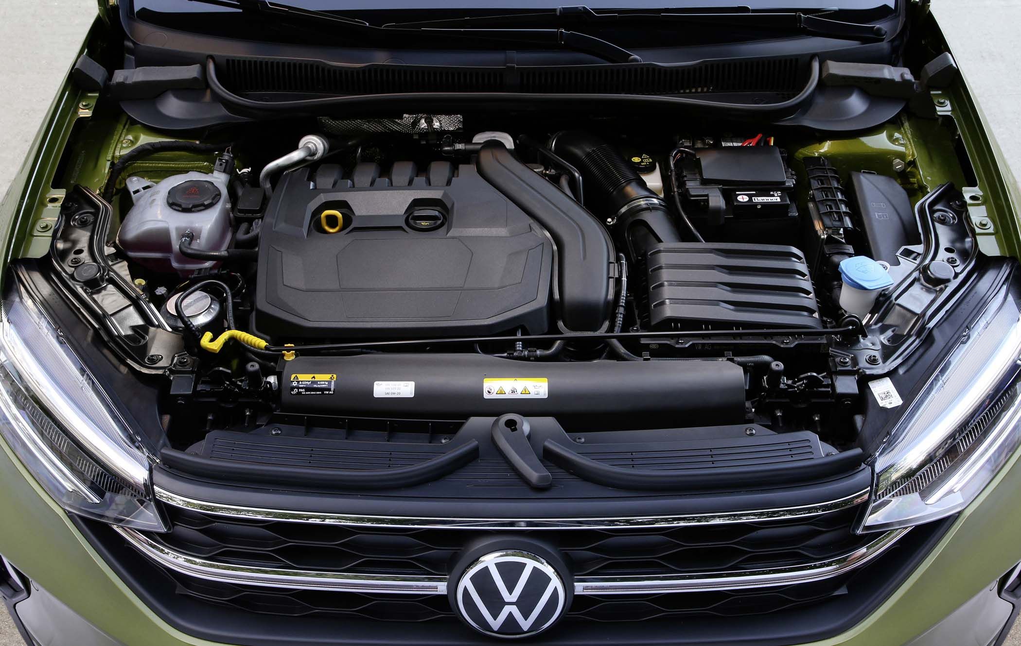 Car engine compartment of a VW Taigo, showing detailed components including a battery, coolant reservoir, and engine cover.