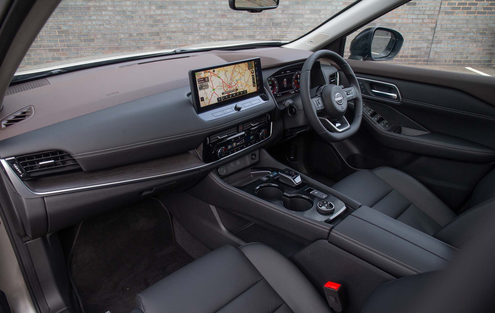 Nissan X-Trail interior with black leather seats, navigation screen displaying a map, steering wheel, and central console with controls and cup holders.