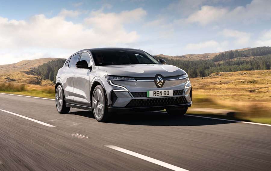 Silver Renault Megane driving on a scenic road with hills and trees in the background under a partly cloudy sky.