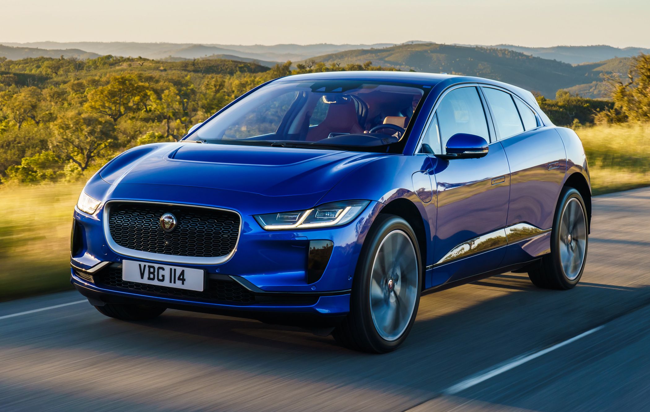 a dark blue jaguar i-pace driving on a sunny country road