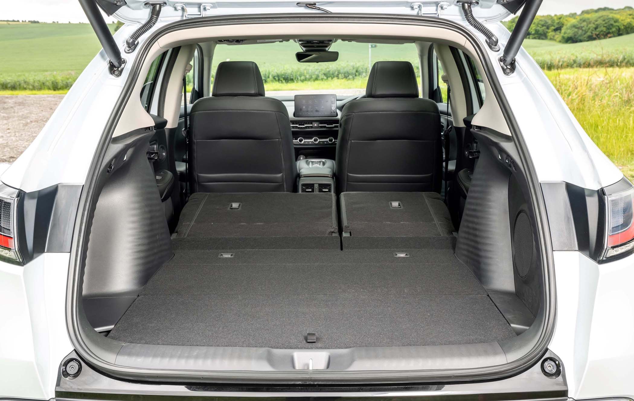 Open boot of a white Honda ZR-V with rear seats folded down, revealing a spacious cargo area. Green fields visible in the background.