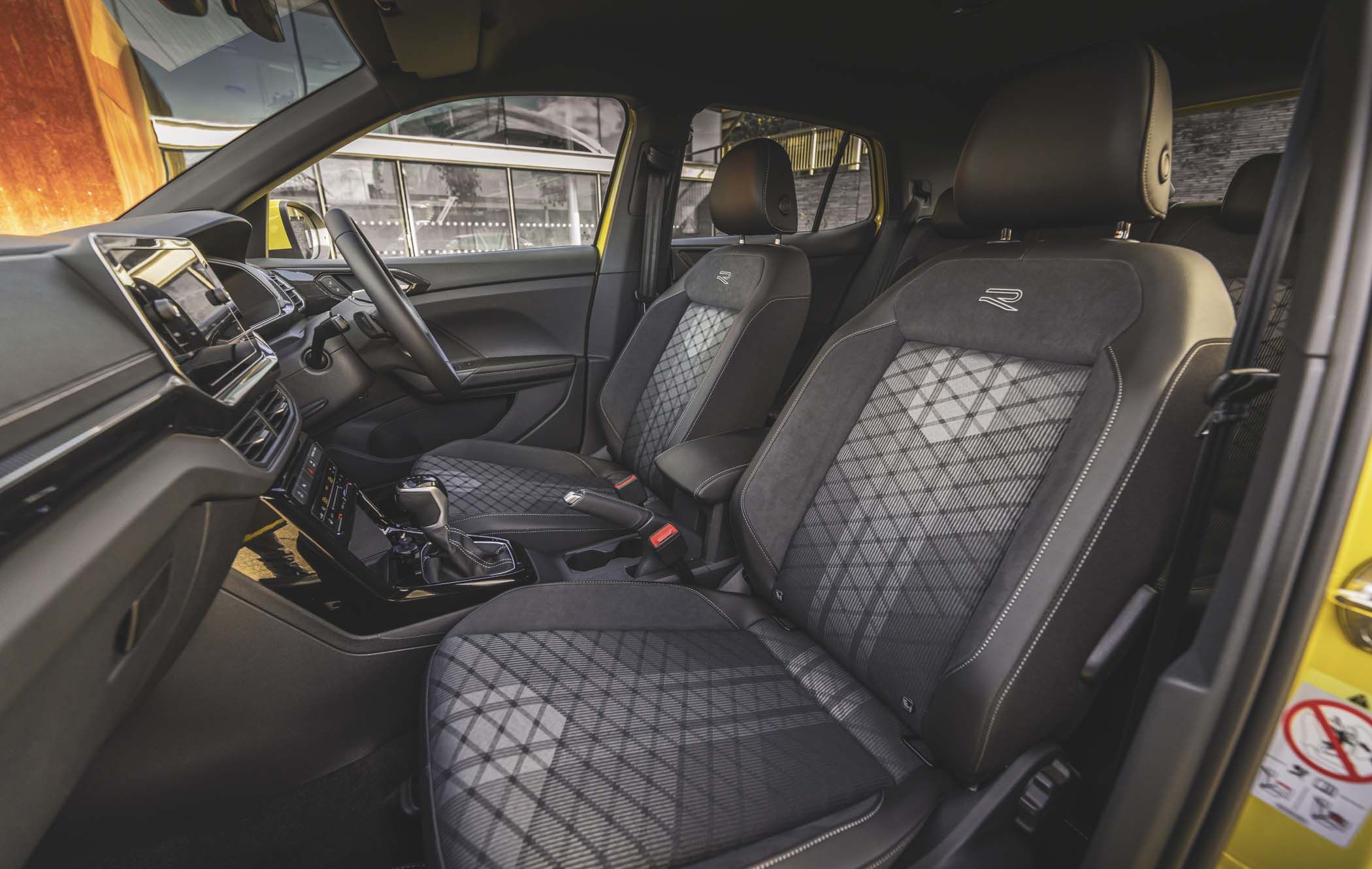 Interior of a VW T-Cross with black and grey patterned seats, a modern dashboard, and a yellow exterior reflected on the door trim.