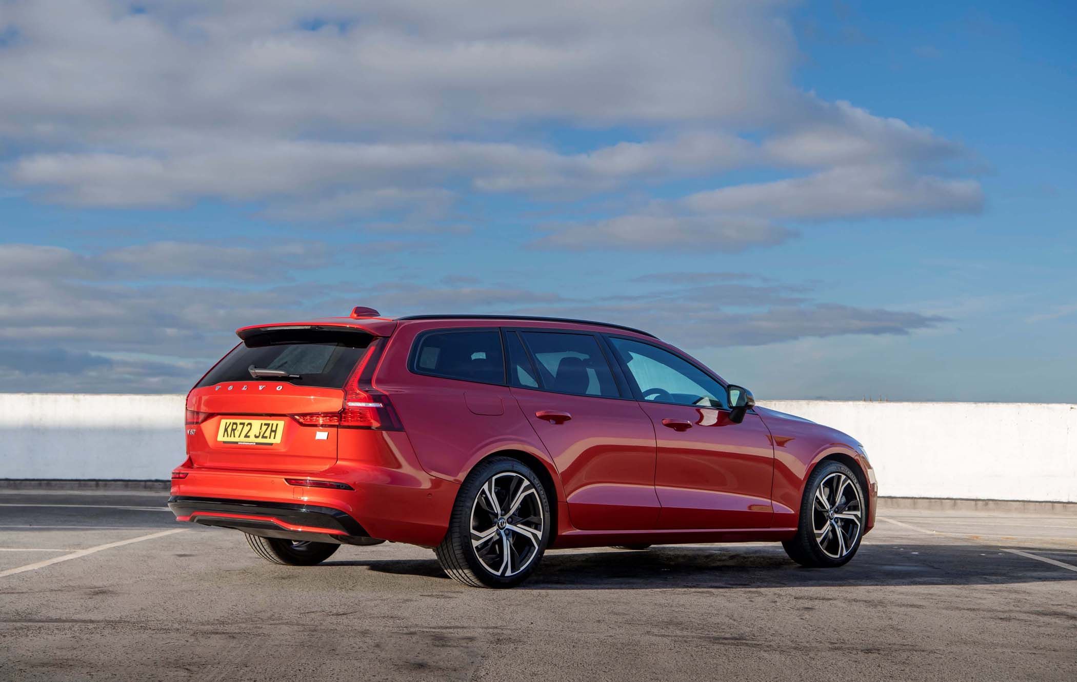 Red Volvo V60 parked on a rooftop with a cloudy blue sky. The car has sleek design and alloy wheels, facing slightly to the right.
