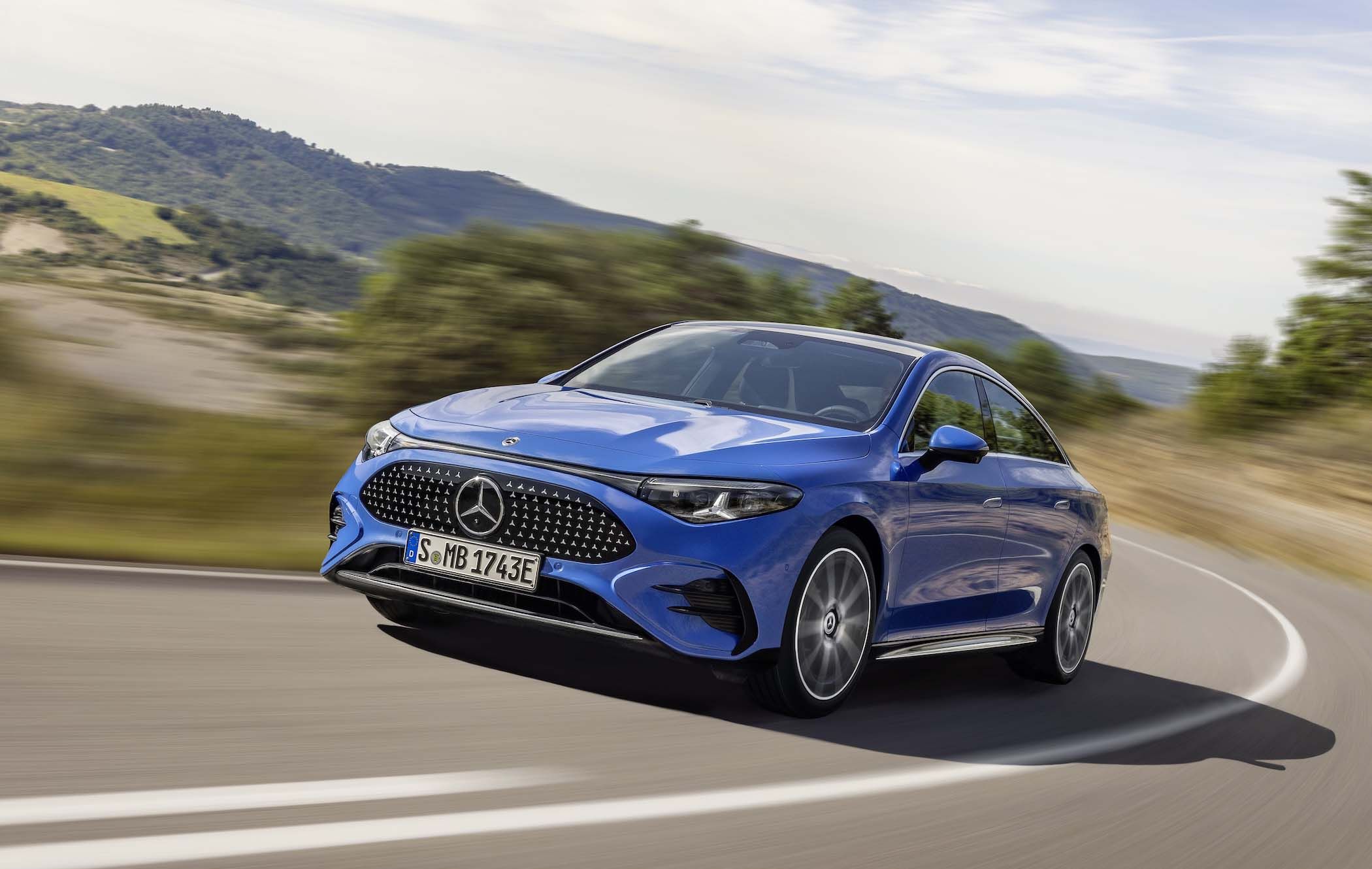 Blue Mercedes CLA driving on a winding road, with blurred greenery and hills in the background under a clear sky.