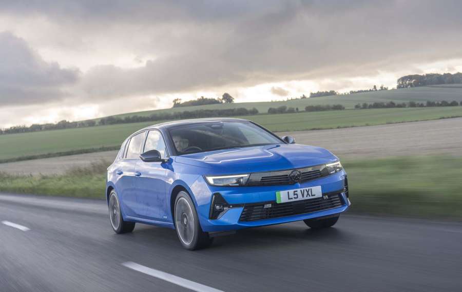 A blue Vauxhall Astra Electric drives on a countryside road with fields and cloudy skies in the background.