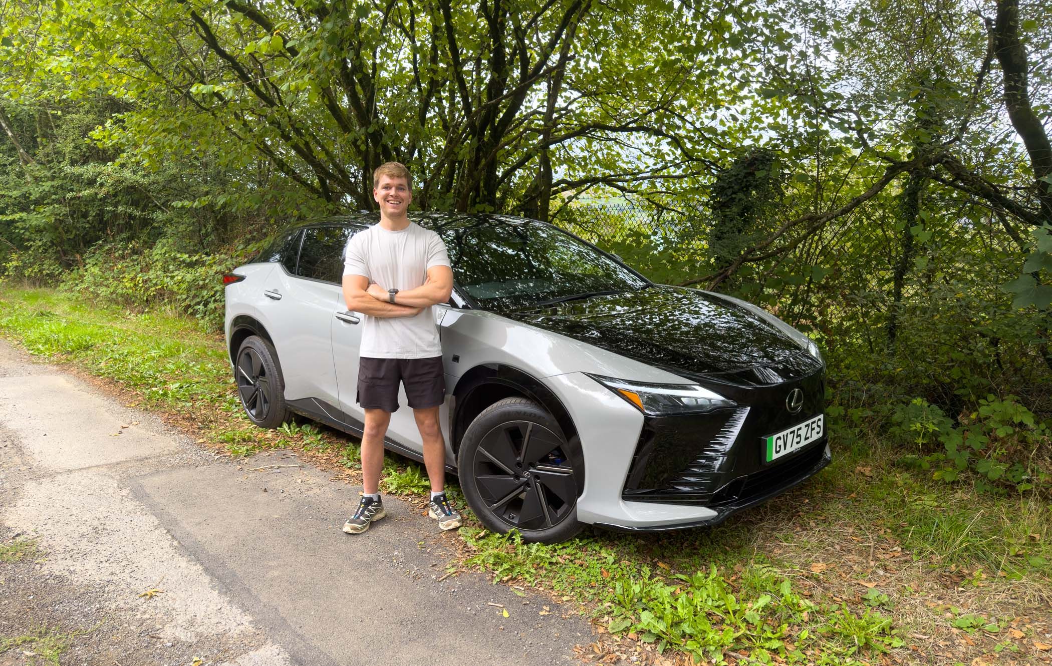 Craig in front of a silver Lexus RZ car parked beside a leafy tree.