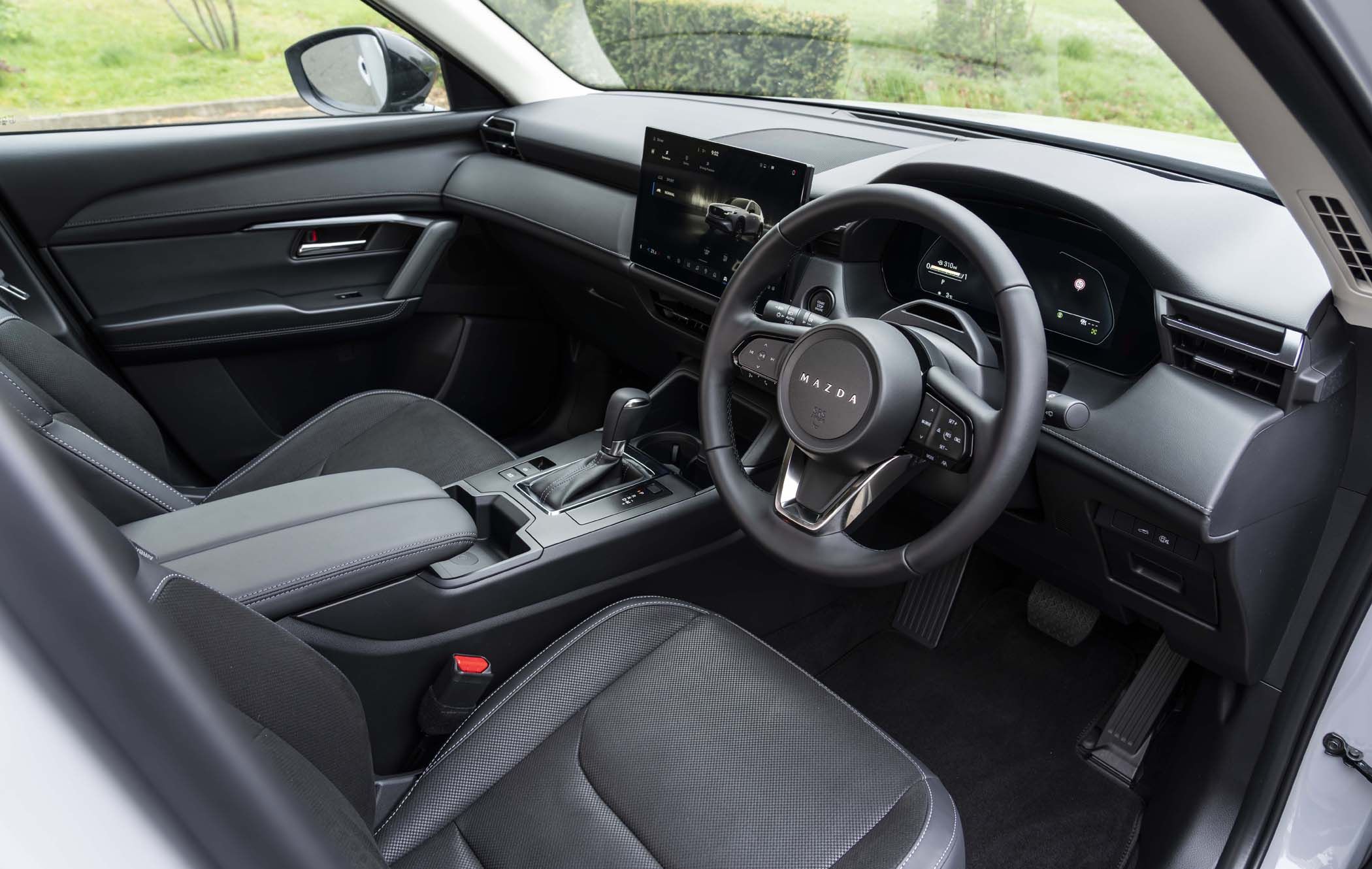 Interior of a Mazda CX-5, featuring a sleek black dashboard, touchscreen display, leather-wrapped steering wheel, and modern controls.