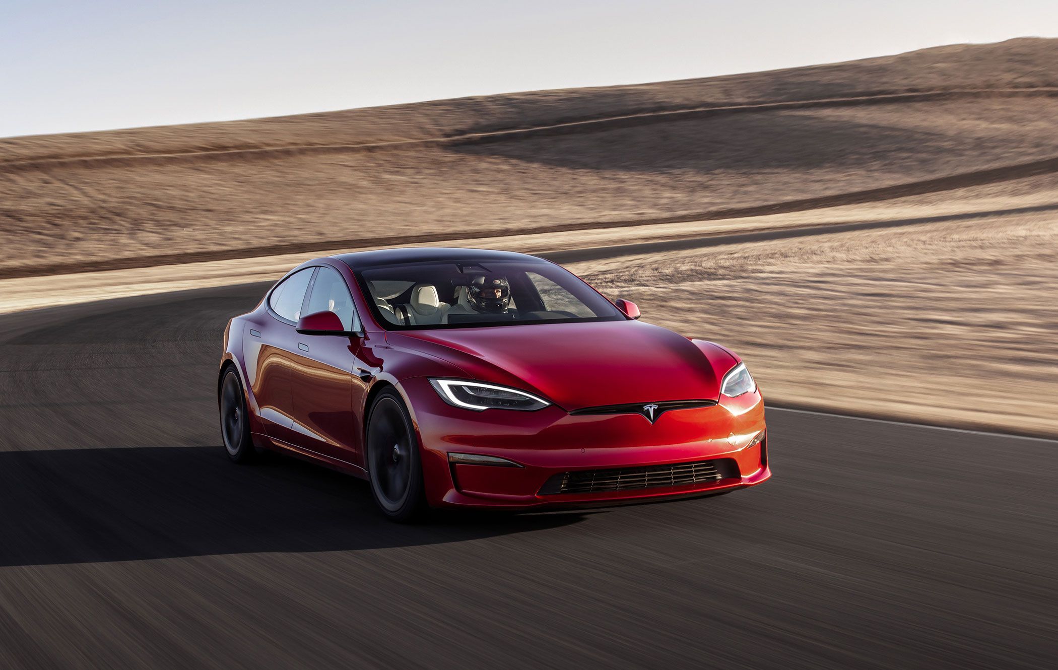 a red tesla model s plaid driving on a racetrack in the desert