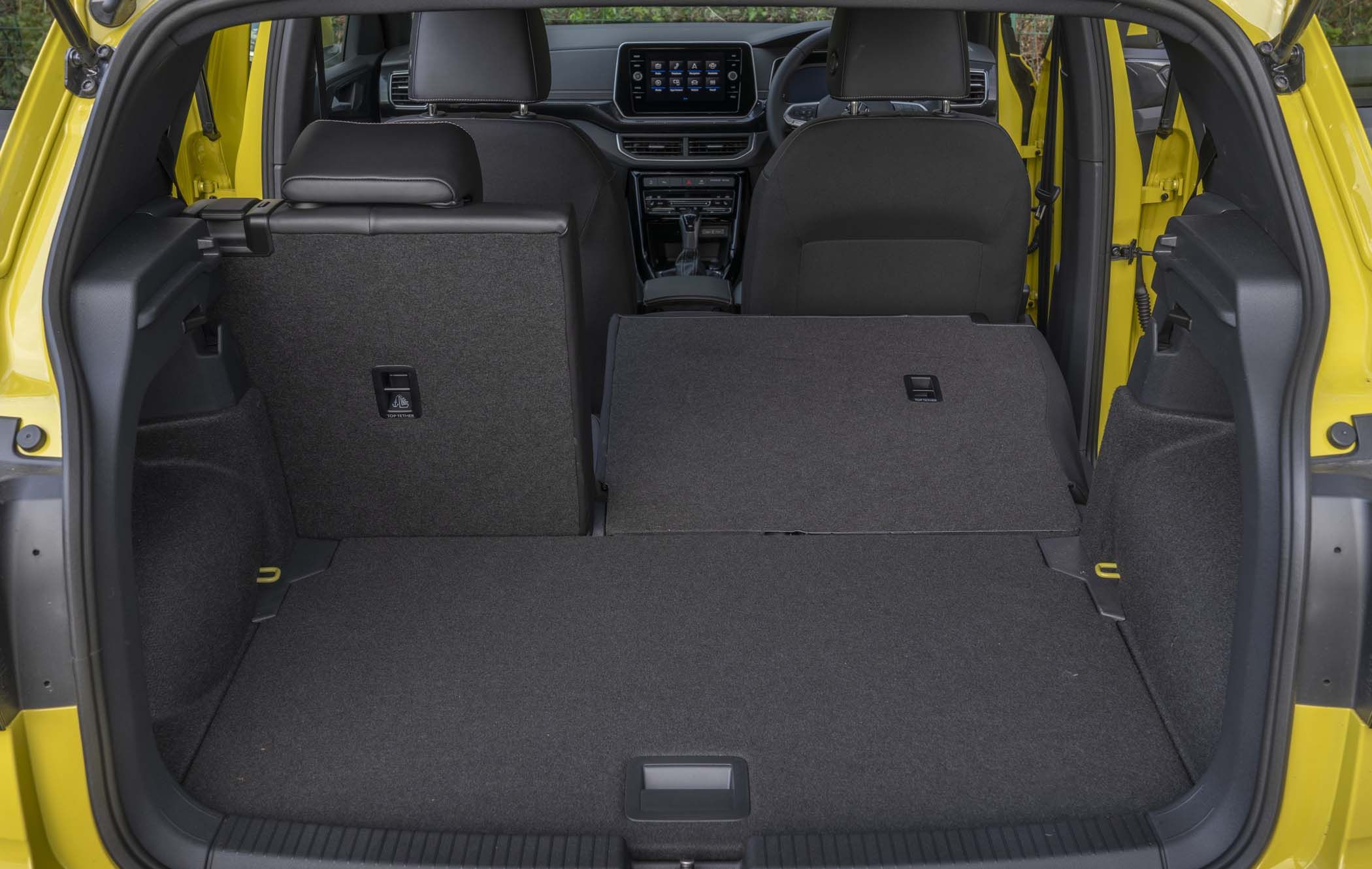 The interior of a yellow VW T-Cross with rear seats partially folded down, showing increased boot space and a view of the dashboard.