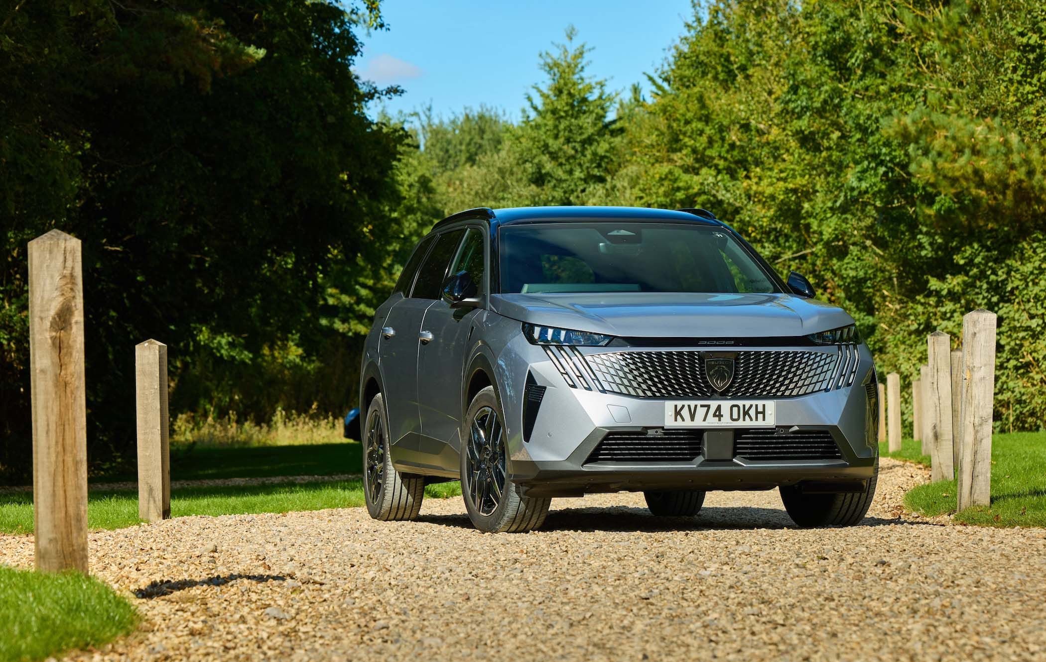 Silver Peugeot 5008 parked on a gravel path, surrounded by green trees and wooden posts, under a clear blue sky.