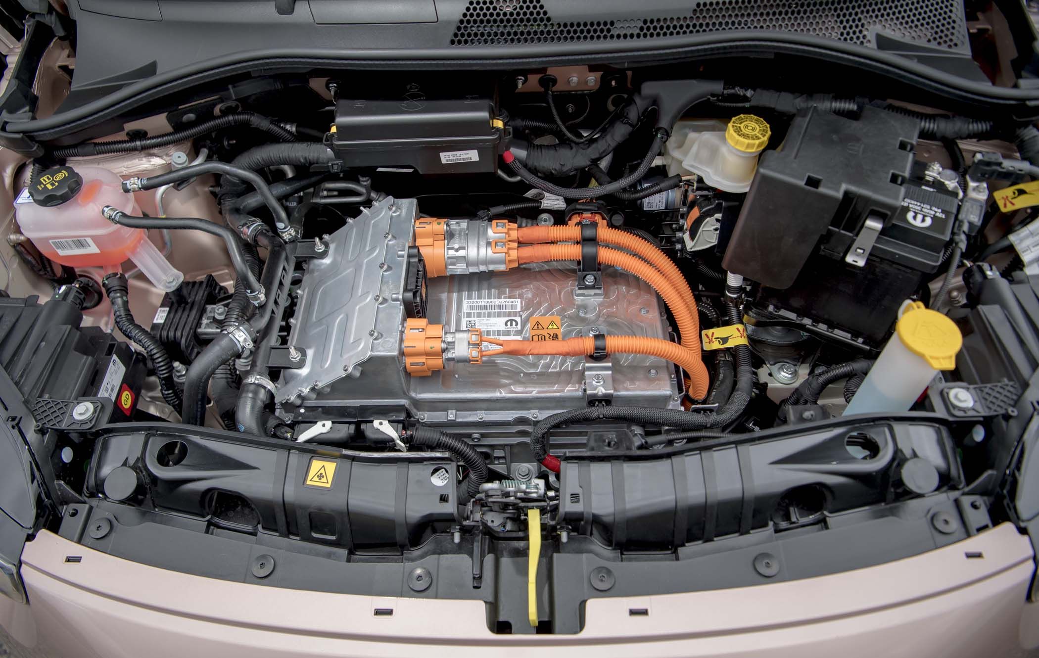 Close-up view of a Fiat 500e electric motor and battery system with orange cables and various components, including a coolant reservoir.