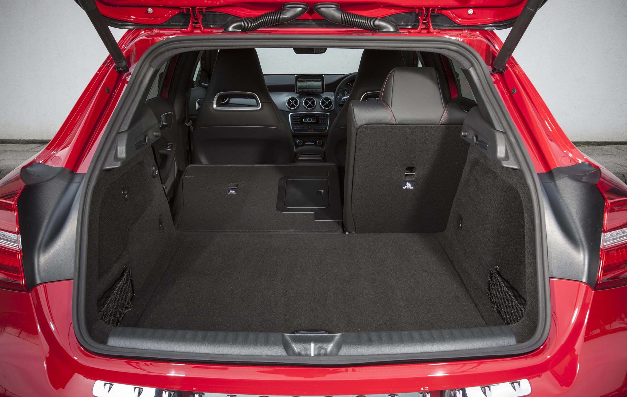 The rear interior of a red Mercedes GLA with seats folded down, showing a spacious luggage area and dashboard controls.