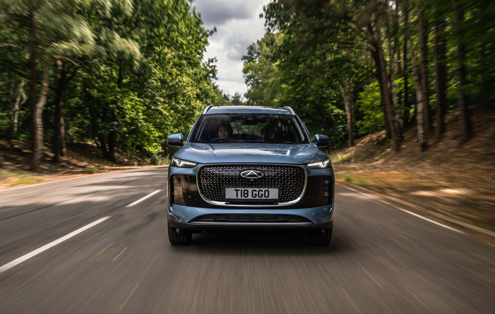 A Chery Tiggo 8 driving on a tree-lined road under a cloudy sky, viewed from the front.