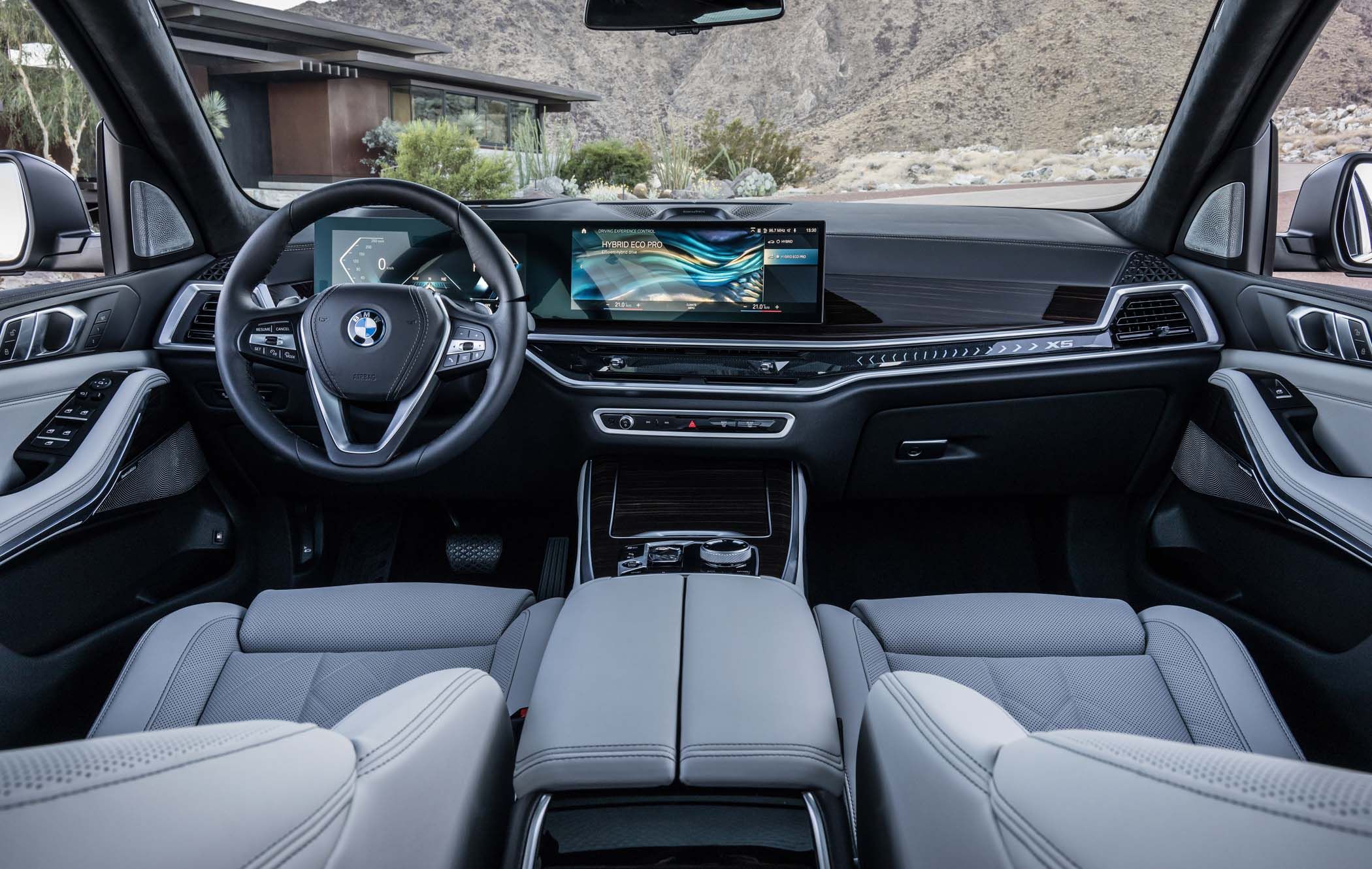 Interior of a BMW X5 with a sleek dashboard, digital display, and leather seats, set against a mountainous landscape visible through the windshield.