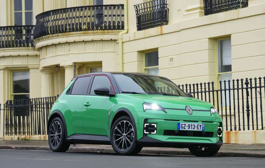 Green Renault 5 parked on a street with ornate black railings and a yellow building in the background.