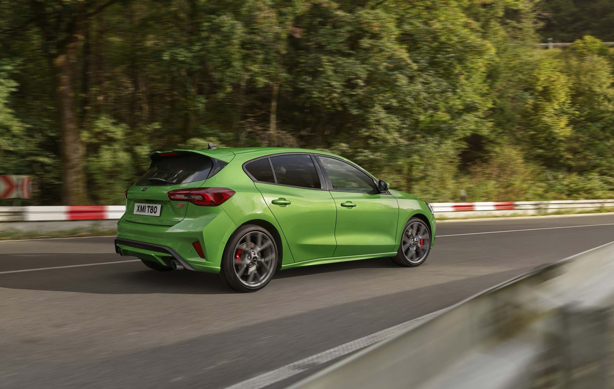 Green Ford Focus driving on a road through a lush forest area, with motion blur indicating speed.