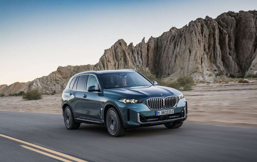 A blue SUV driving on a desert road with rocky cliffs in the background under a clear sky.