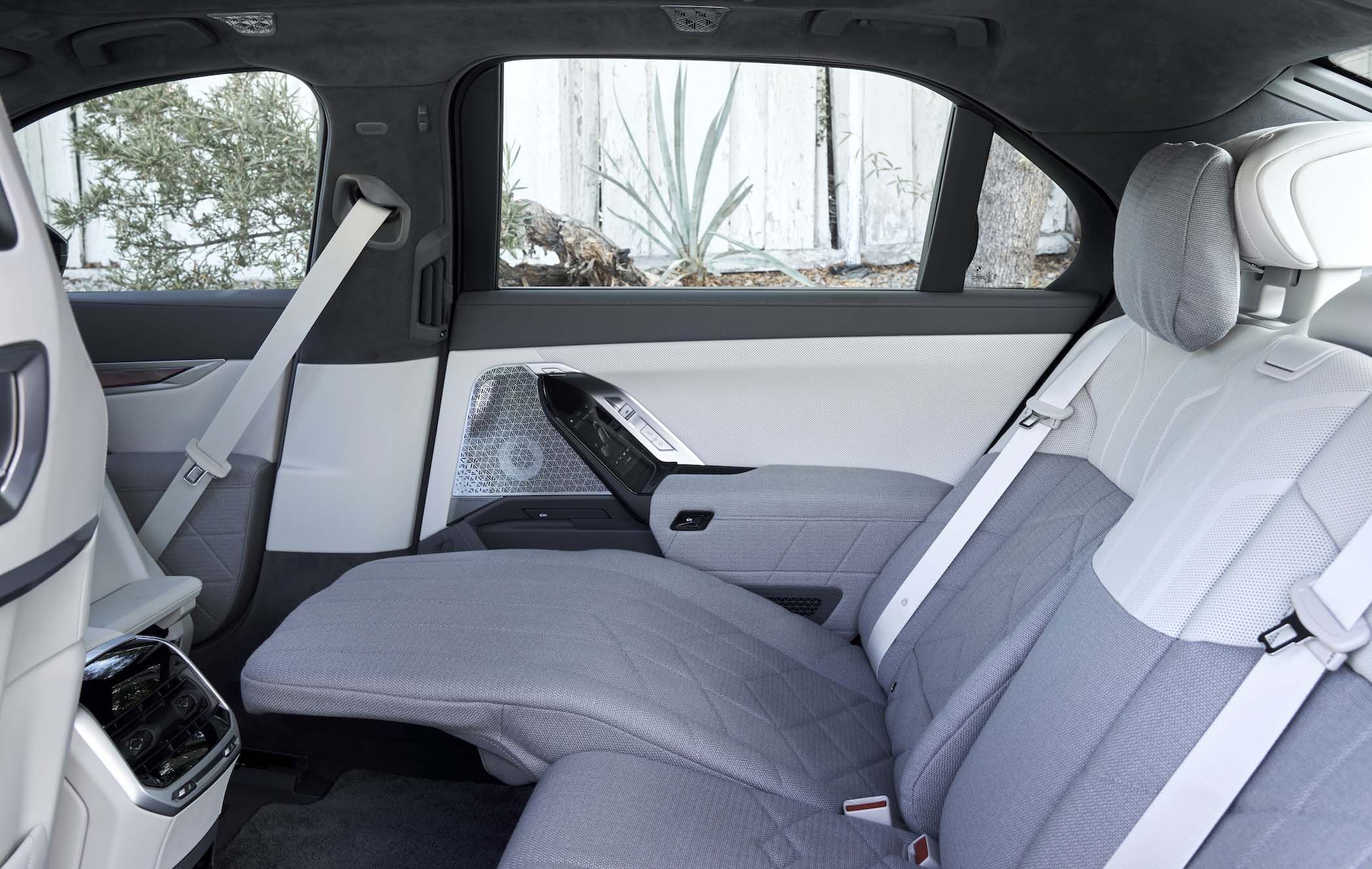 BMW 7 Series interior with light grey upholstery, spacious backseat, and modern design. Features include a center console and sleek door panel.