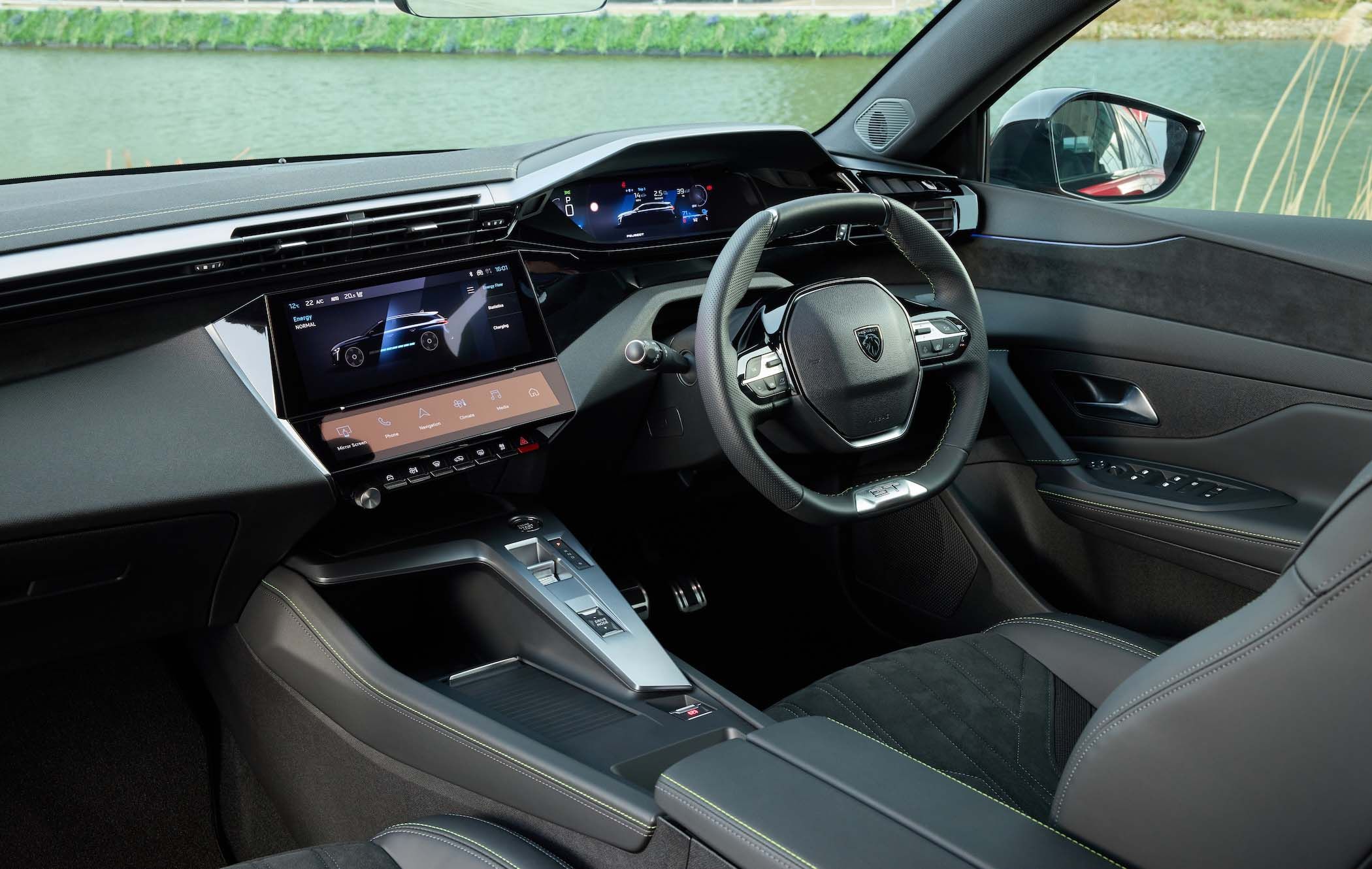 Peugeot e-308 SW interior featuring a sleek dashboard, digital displays, multifunction steering wheel, and black leather seats by a water view.