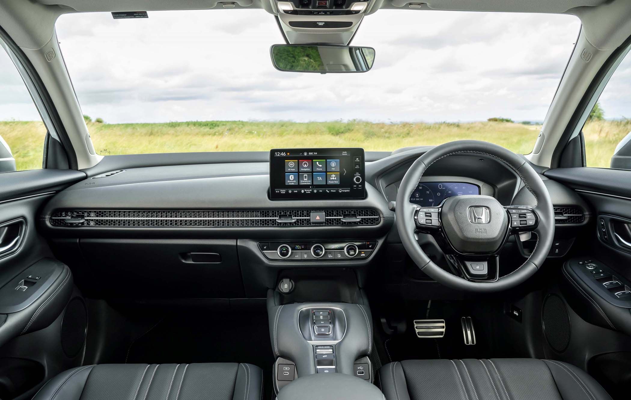 Interior of a Honda ZR-V featuring a sleek dashboard, touchscreen display, multifunction steering wheel, and leather seats, with a view of a grassy field.