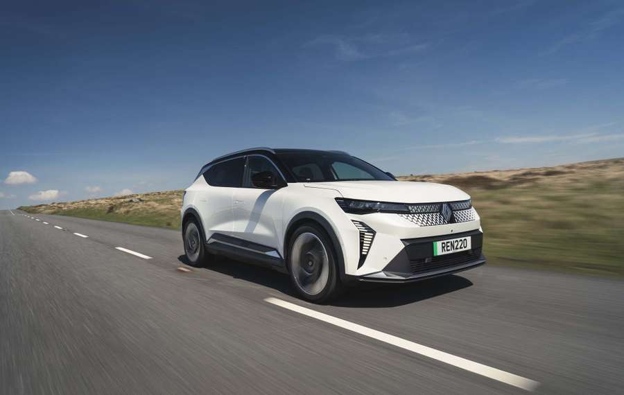 A white Renault Scenic with a sleek design driving on an open road under a clear blue sky.