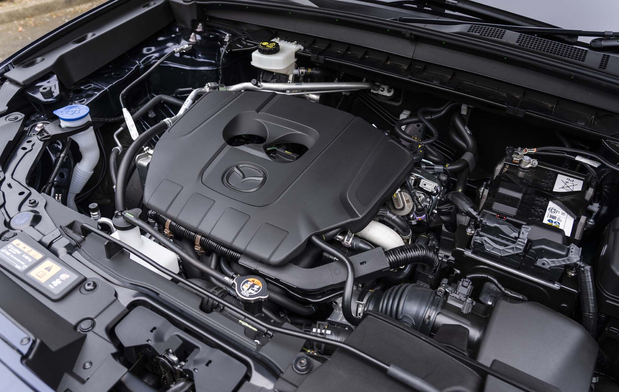 View of a Mazda CX-5 engine bay showcasing a covered engine, battery, and various components, with visible branding on the engine cover.