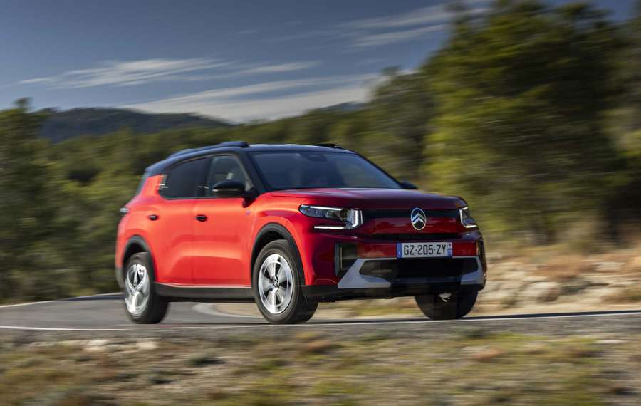 Red Citroën ë-C3 Aircross driving on a curvy road with blurred greenery in the background, under a clear blue sky.