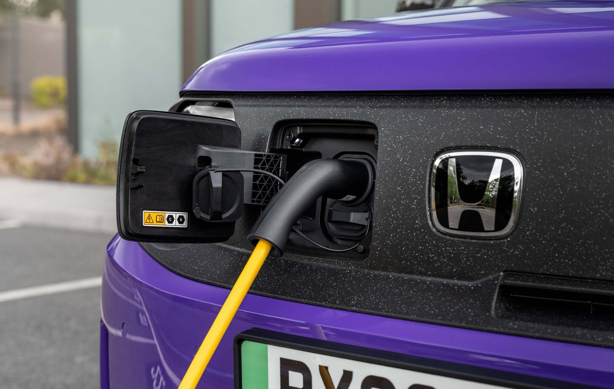 Close-up of an electric car charging port on a purple Honda Super-N with a yellow cable plugged in.