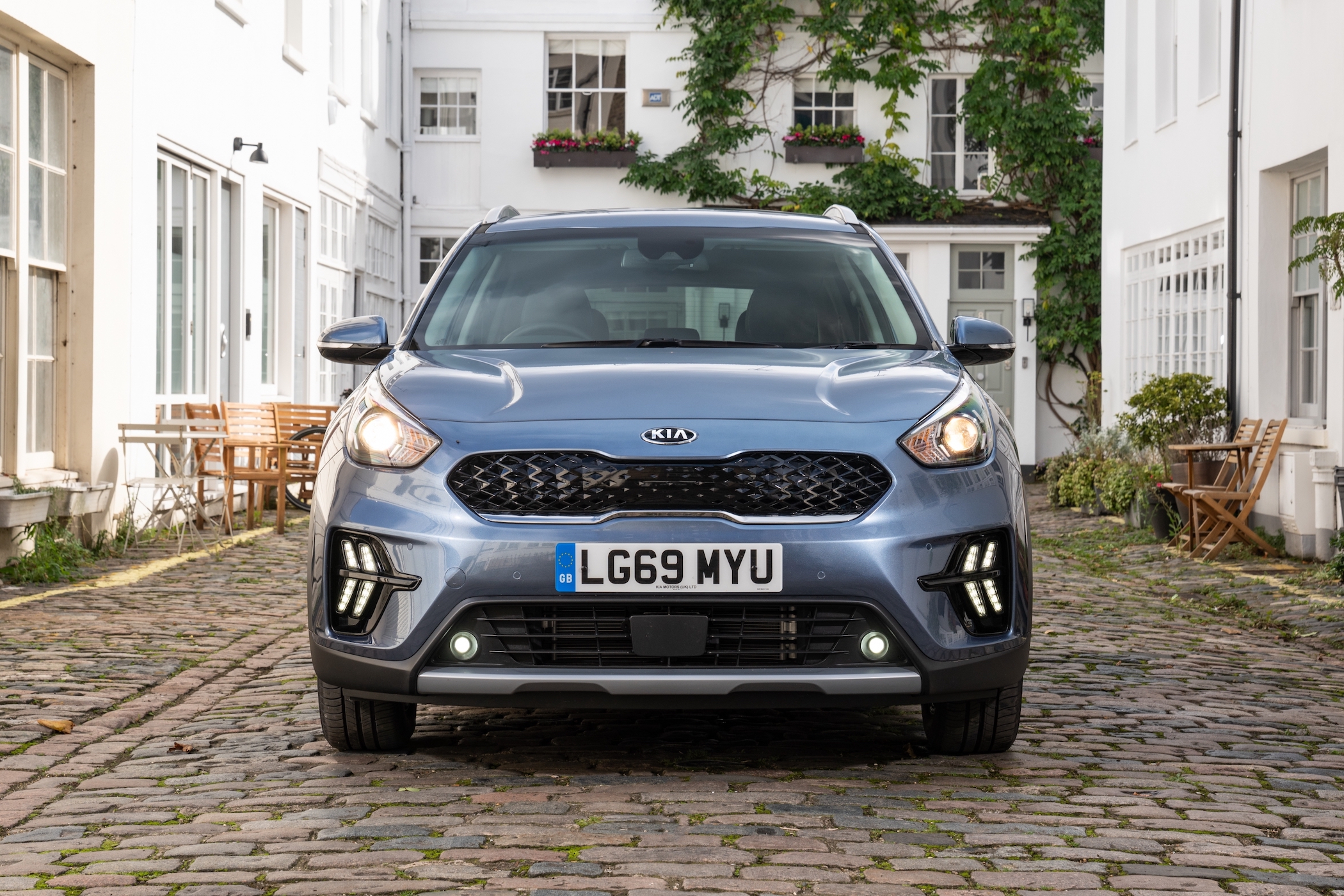 a blue kia niro parked next to a london mews house
