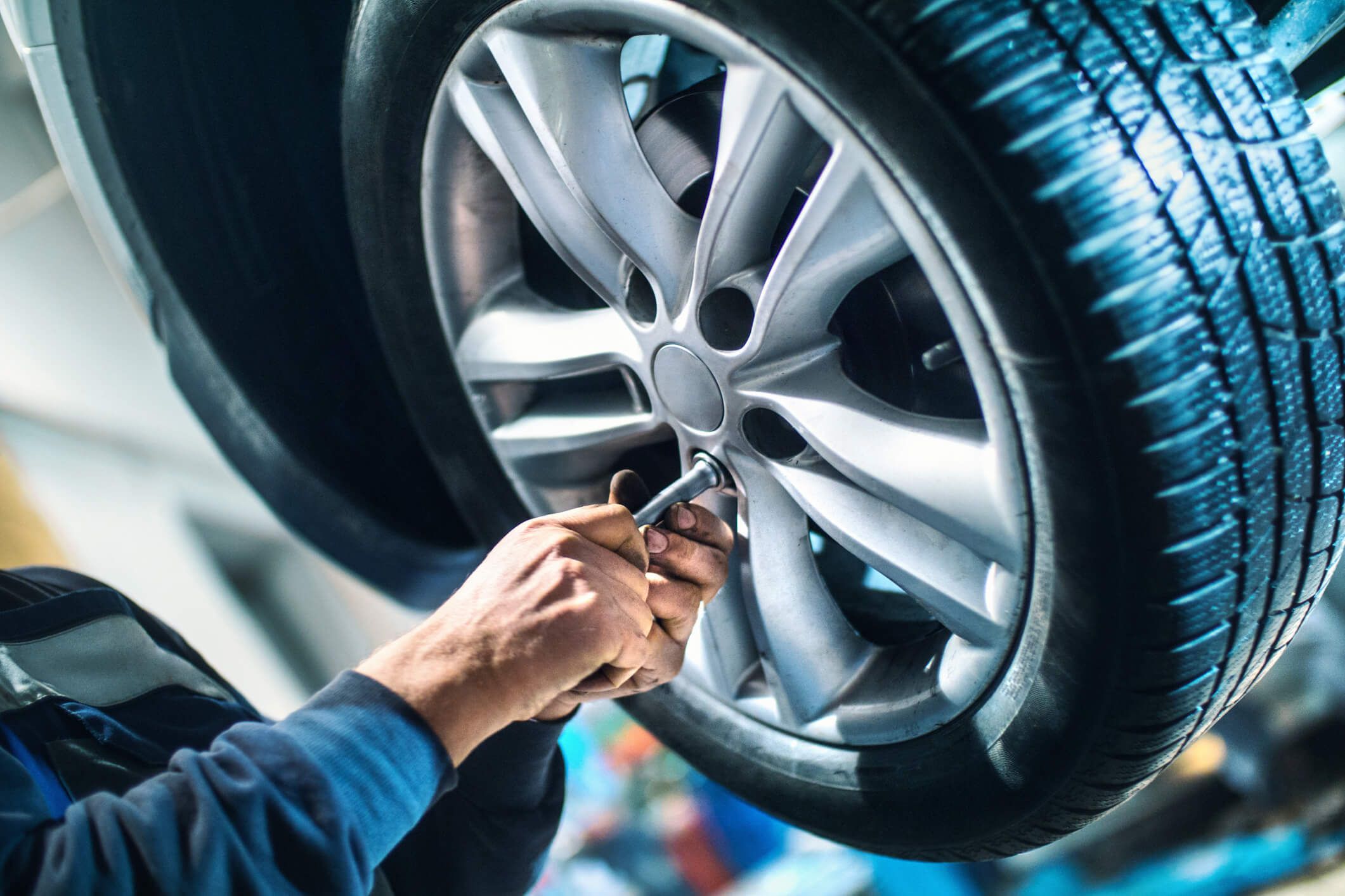 A hand using a tool on a car wheel in a garage