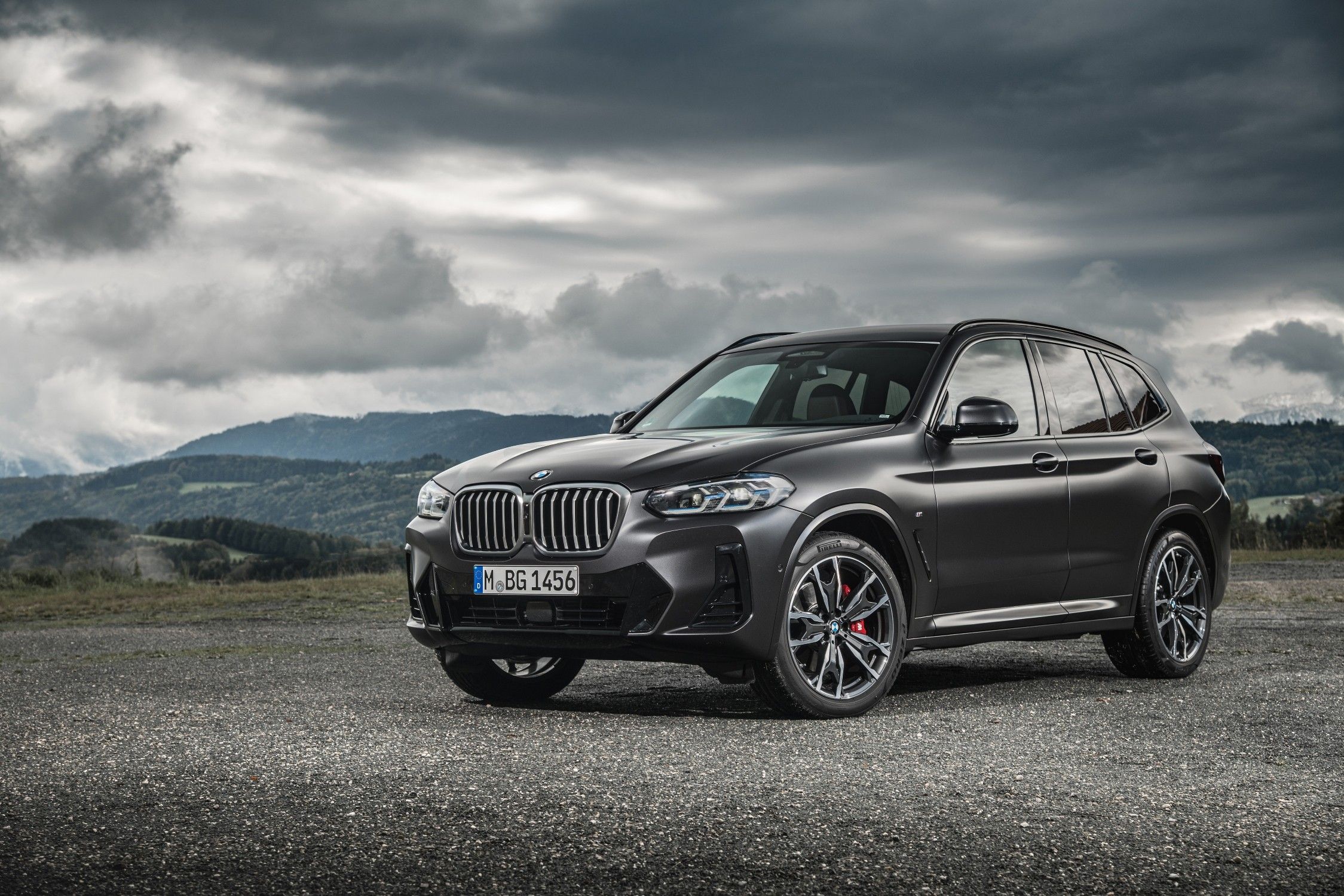 A black BMW X3 parked on gravel next to some mountains with a cloudy sky