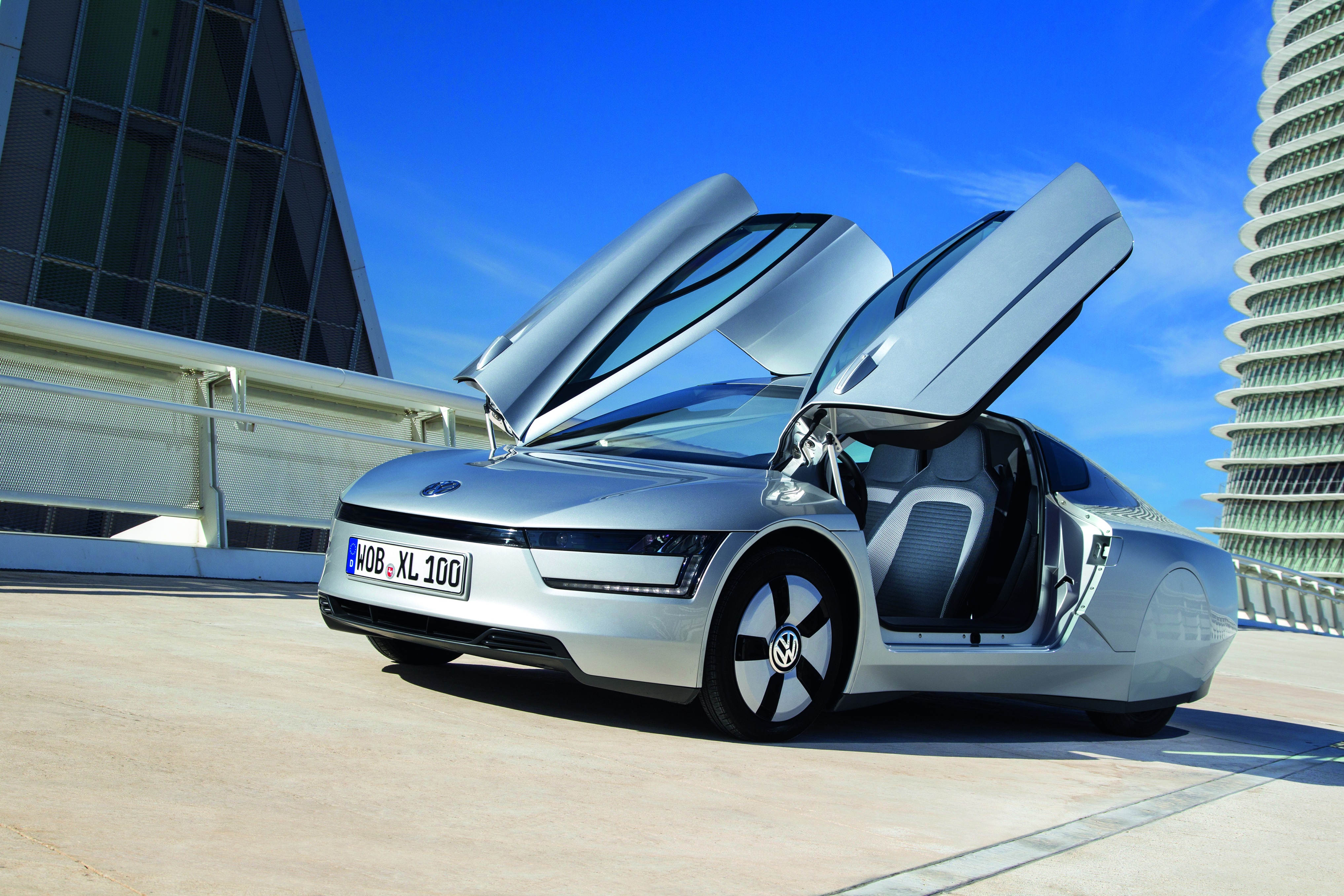 a grey vw xl1 with its doors open parked on a rooftop road