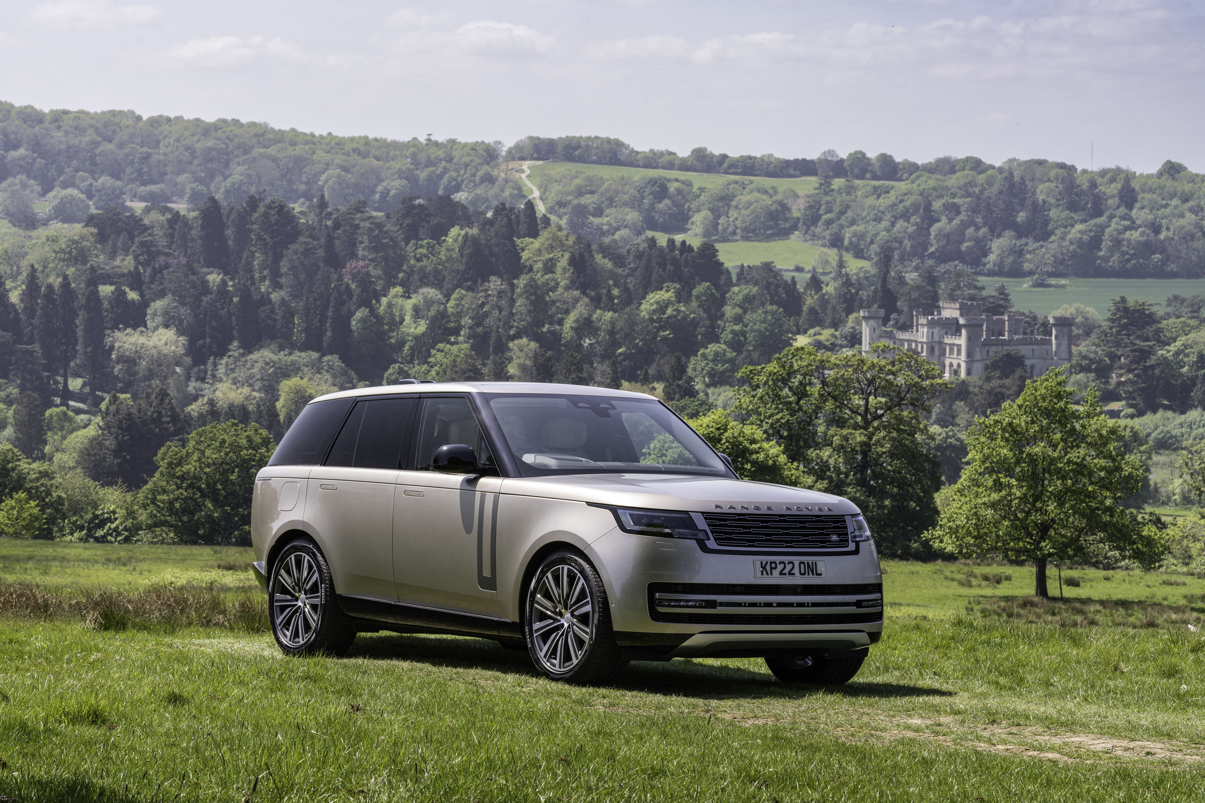 a gold range rover parked on grass in front of a hill