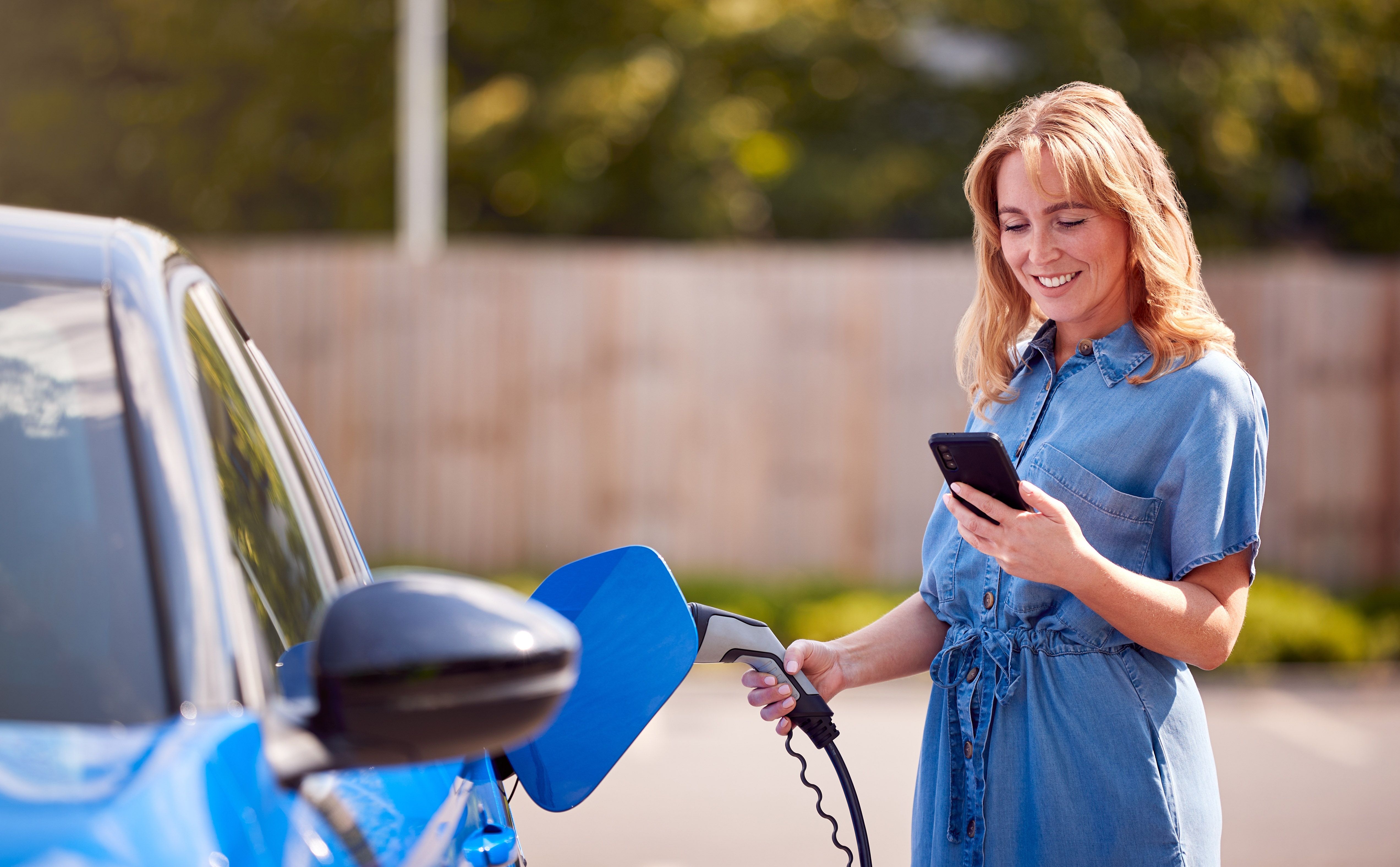 A woman checking her phone while charging an electric car