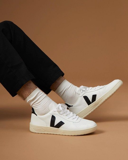 Studiofoto bruine achtergrond met witte VEJA V10 sneakers met zwarte details