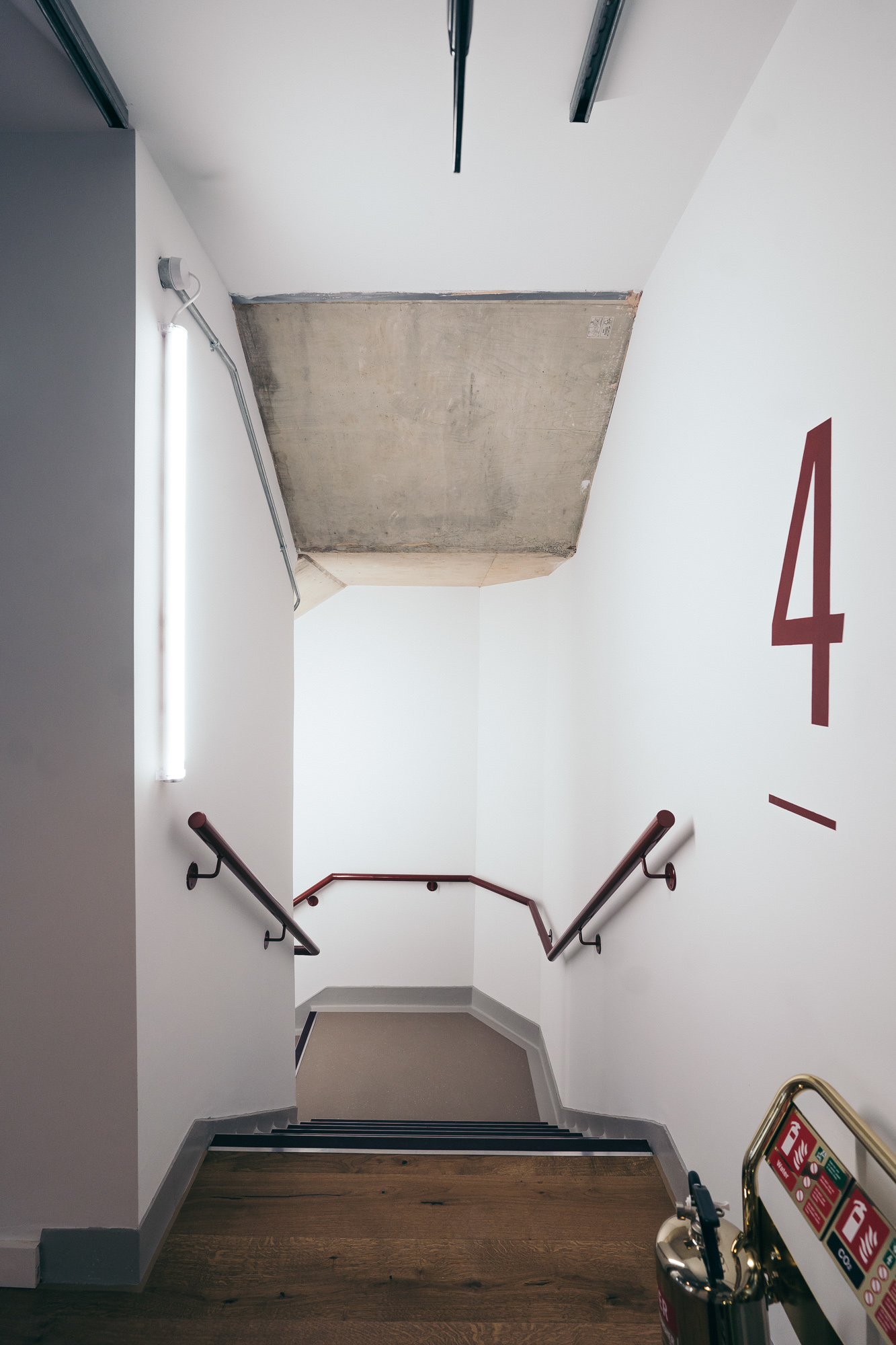 Stairwell with white walls, red handrails, and a large red number 4 on the wall. A fluorescent light is on the left side, lighting up this little corner of Leroy House.