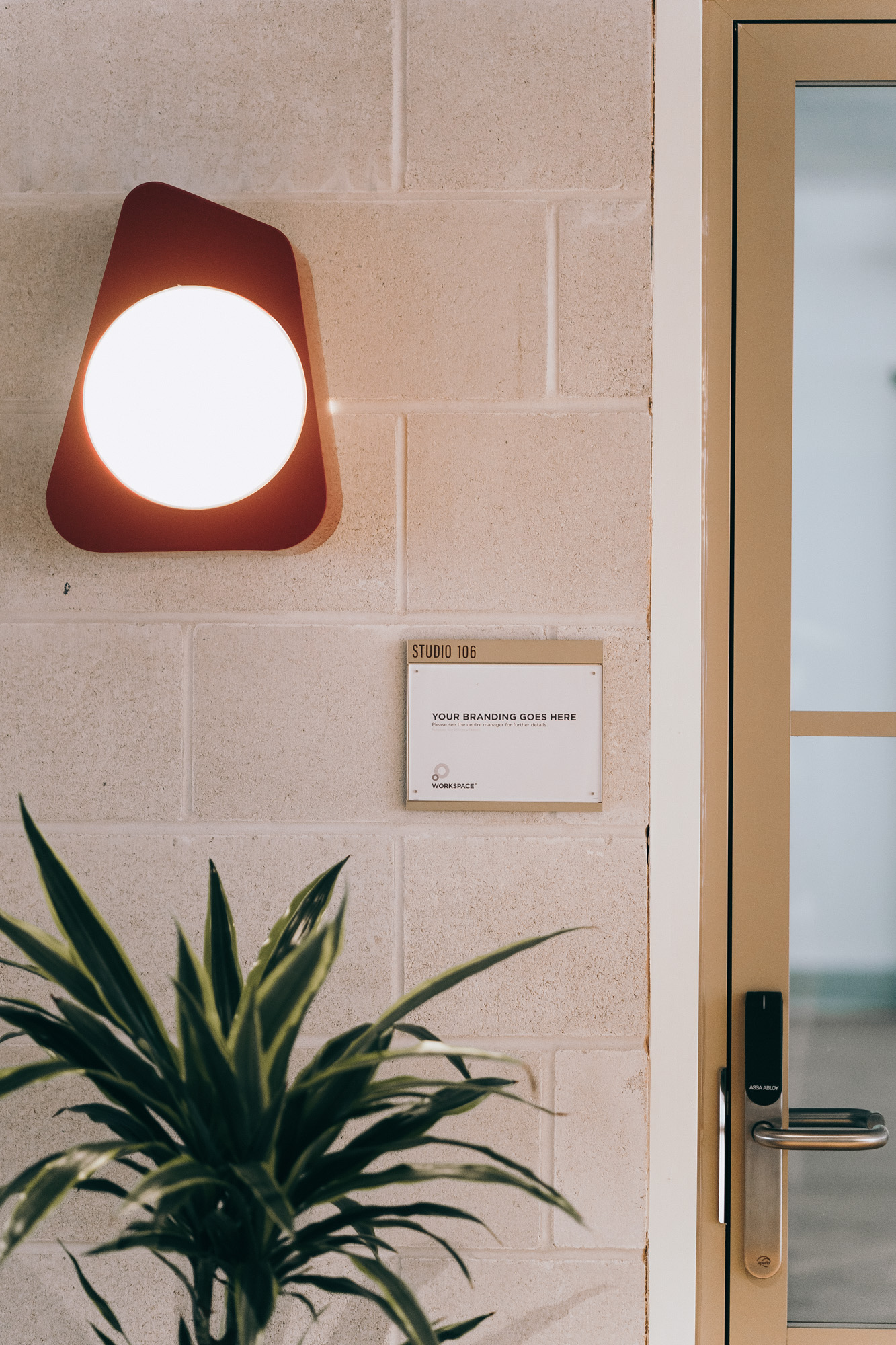 Wall with a modern triangular light, an acrylic slider sign labeled "Studio 106," and a potted plant - making up the modern aesthetic of Leroy House.