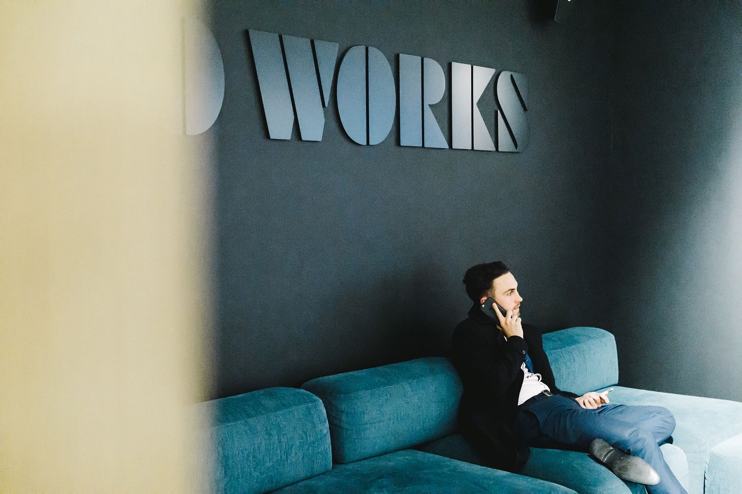 Very large black MDF 3D lettering spelling CARGO WORKS fixed on a black wall above a visitor sitting in a reception area