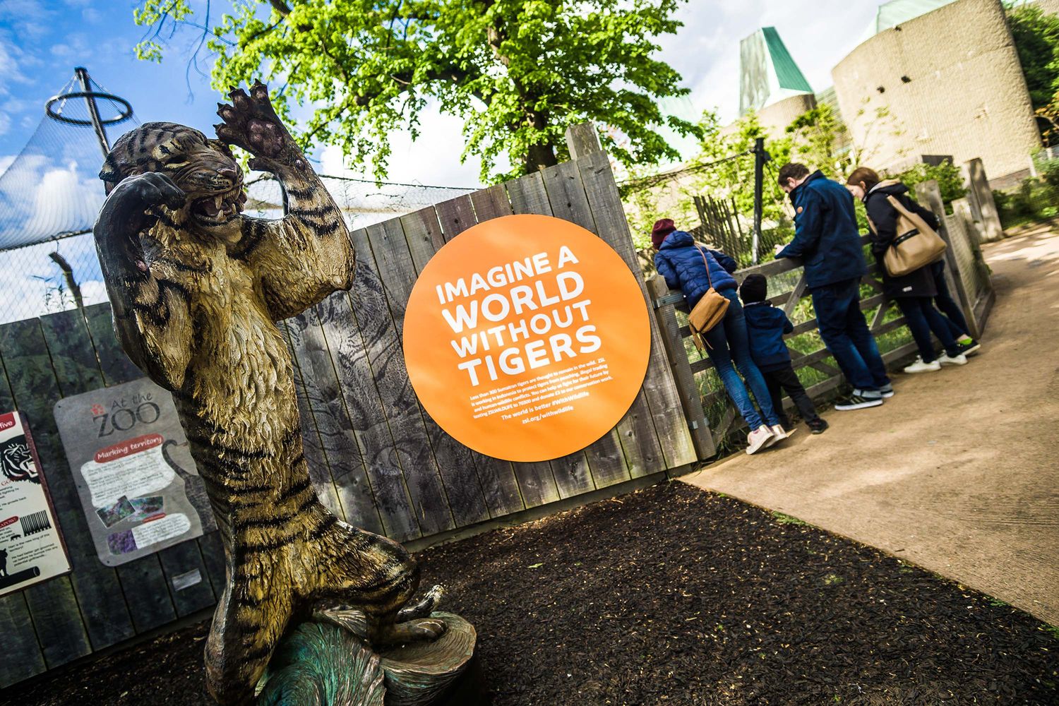 A large round orange sign made from aluminium composite placed on a fence indicates the tiger enclosure at London Zoo. Cultural signs can be bold.