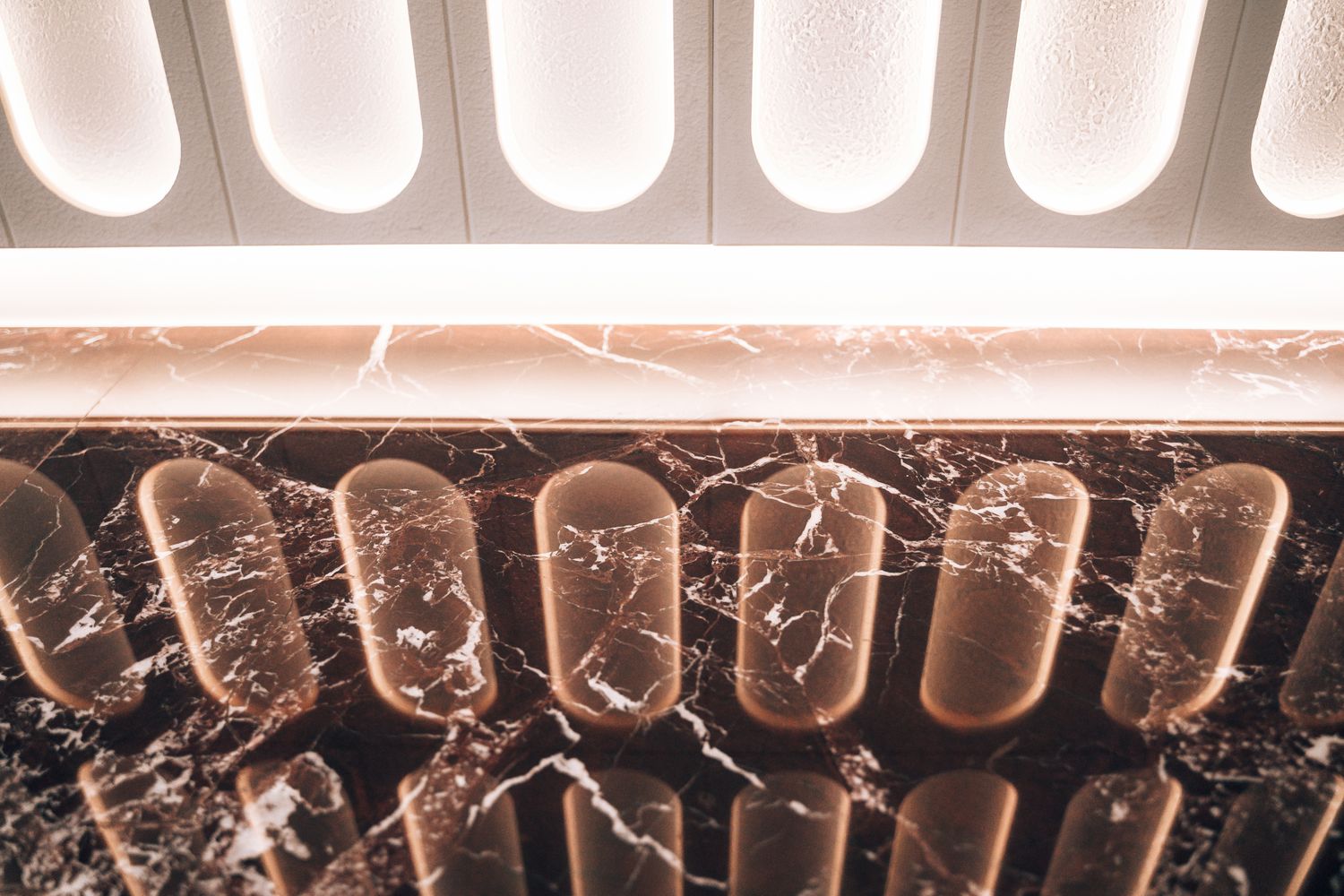 Close-up of the illuminated reception wall at Ellisse by Spacemade, showing a reflection of the repeated ellipse forms and halo lighting.