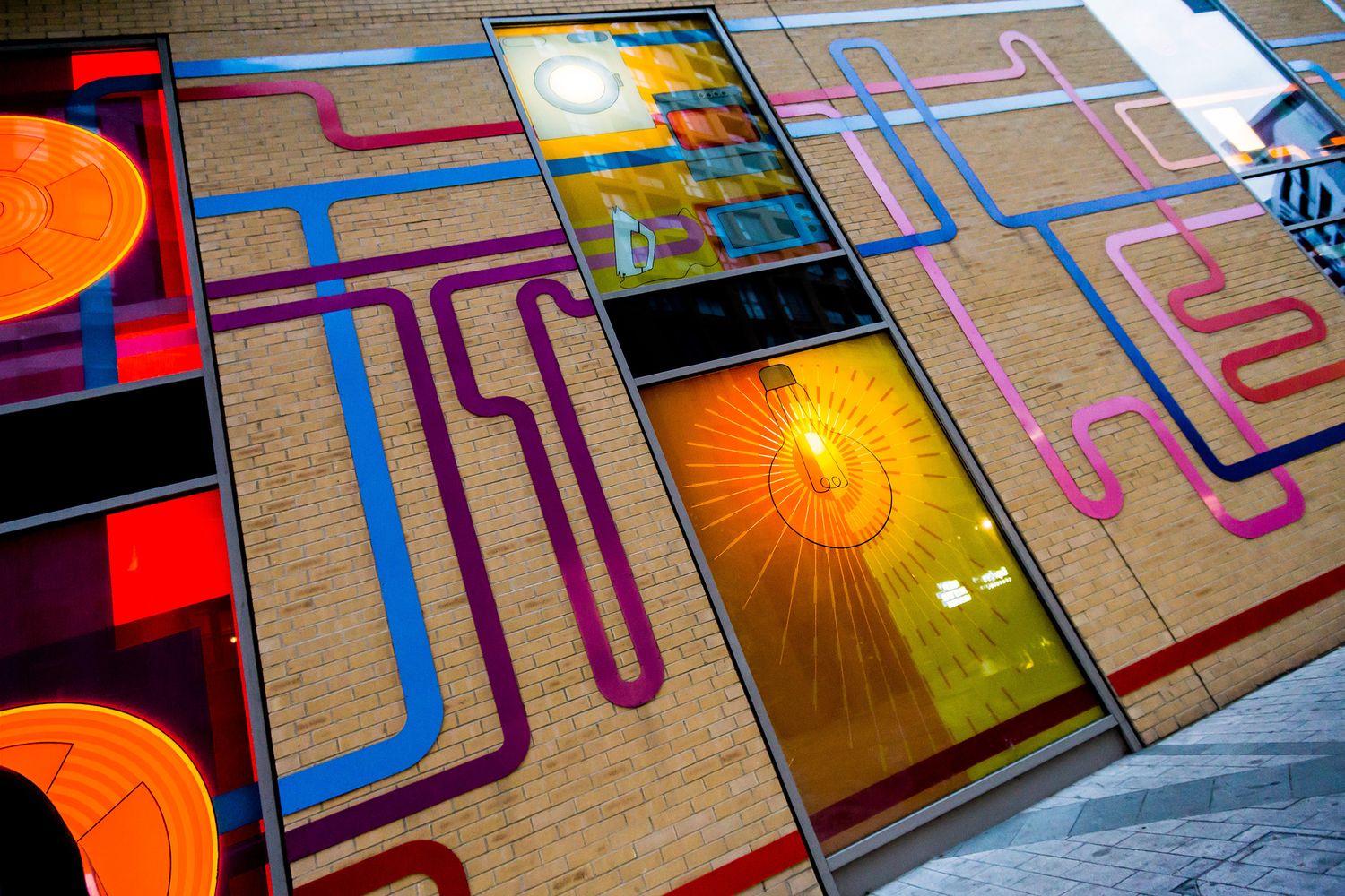 A close up of the Barratt Homes energy centre outside wall showing a large architectural sign representing a network of colourful acrylic 2D pipes snaking along the walls