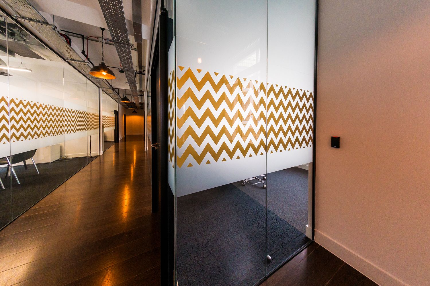 A corridor view showing how the light flows through the glass meeting room wall where bespoke manifestations have been applied.