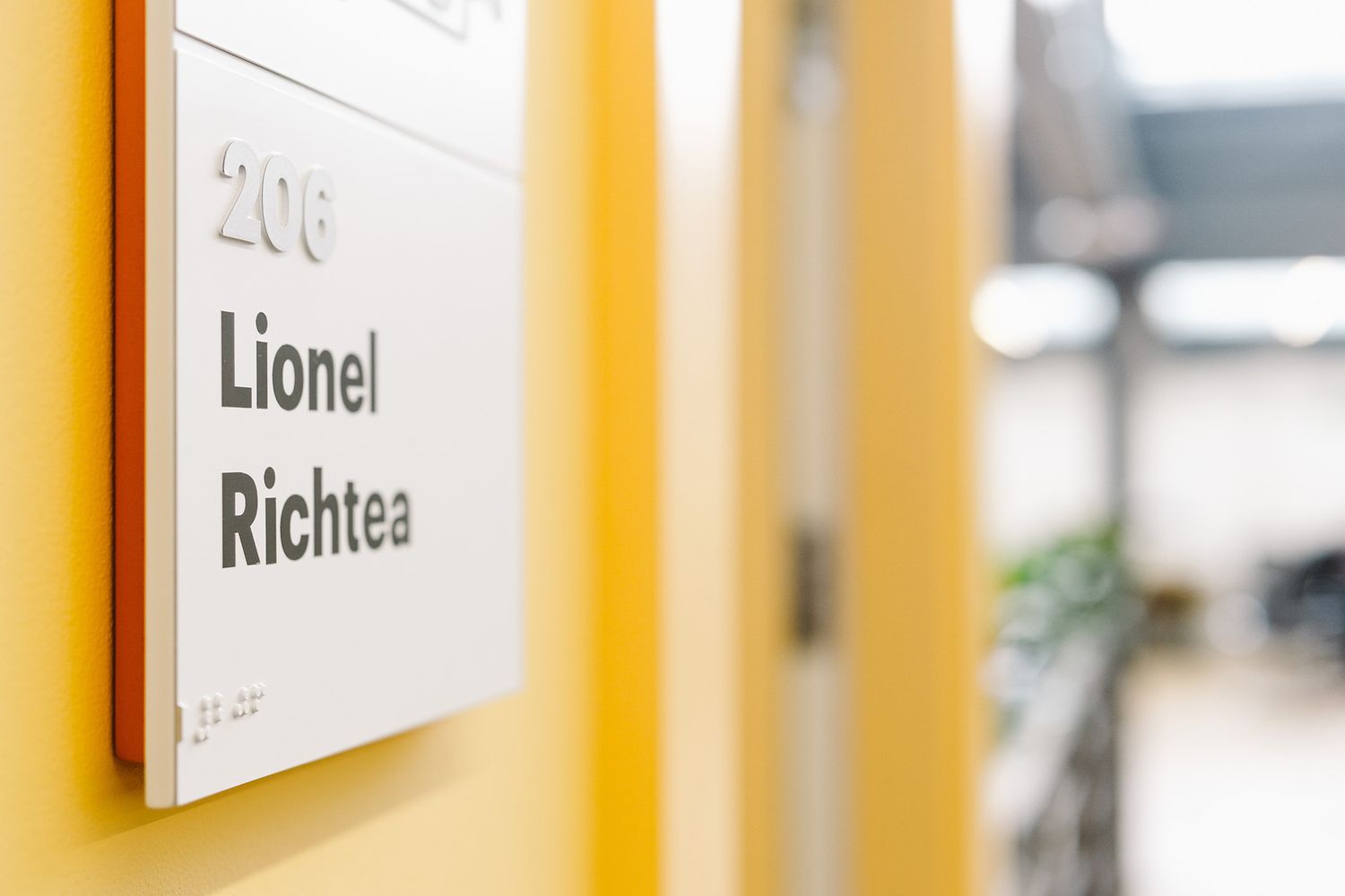 Picture of an orange, white and grey lettering braille wayfinding sign for a meeting room called Lionel Richtea at Easy London offices