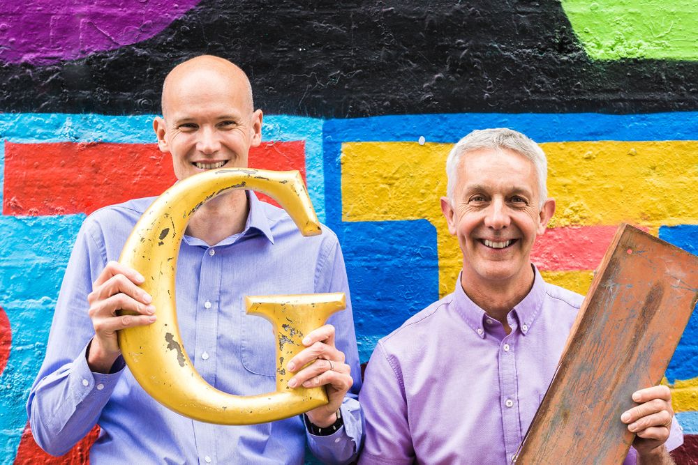 Tim holding a large golden wooden G and Paul an old I metal sign