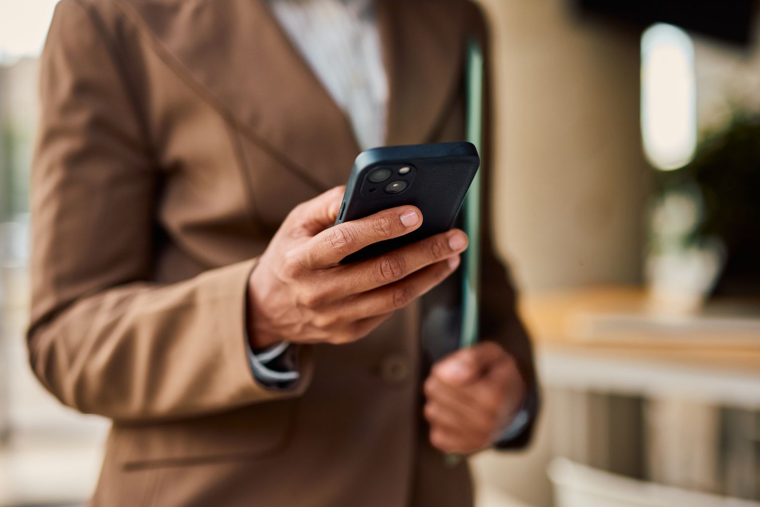 Person im Businessanzug bedient ein Smartphone, im Hintergrund ein Büroumfeld – symbolisiert mobile Freigabe von Kartentransaktionen.
