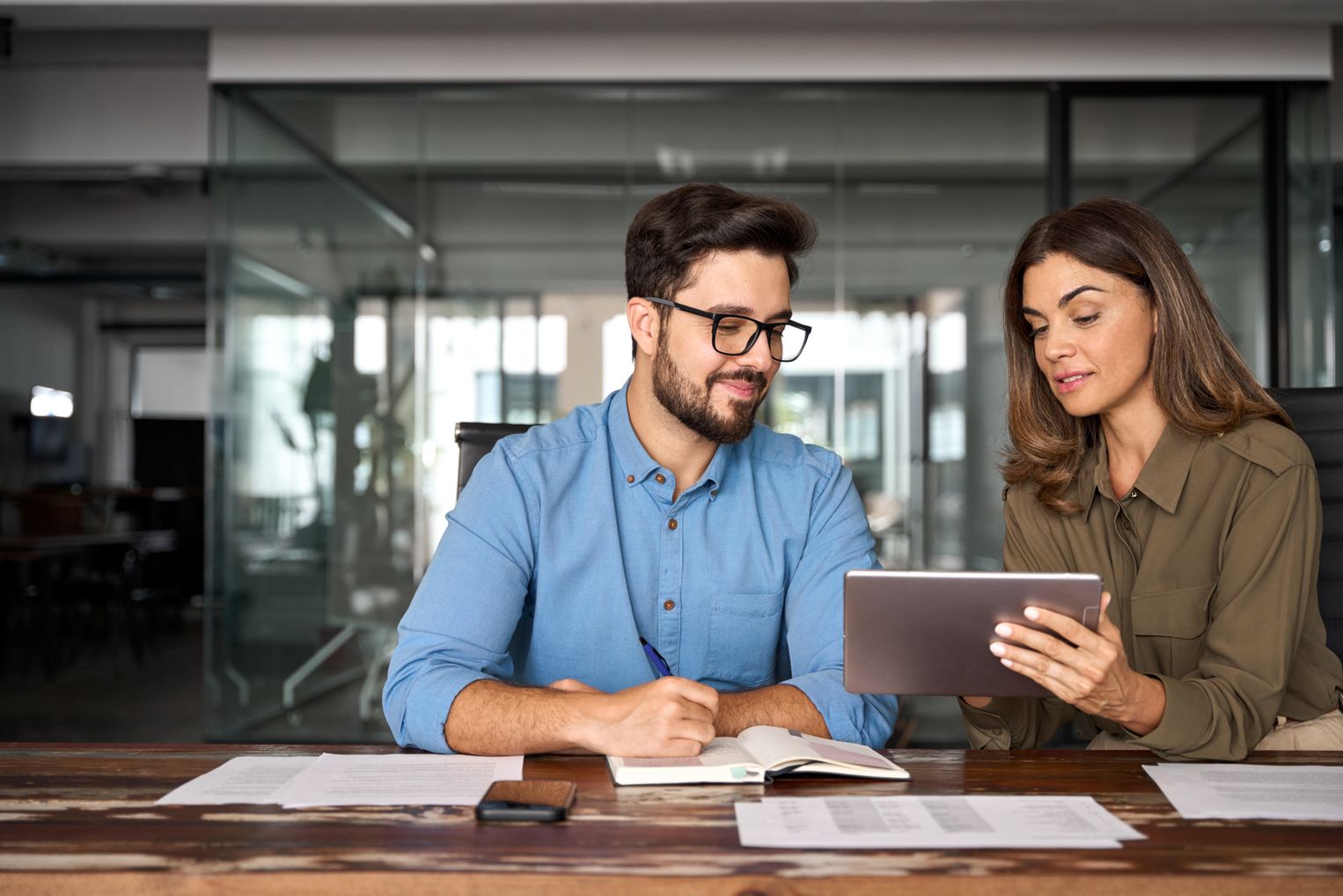 Buchhalter und Kollegin sitzen gemeinsam am Schreibtisch und prüfen E-Rechnungen auf einem Tablet – Finanzteam bei der Umsetzung der E-Rechnungspflicht 2025.